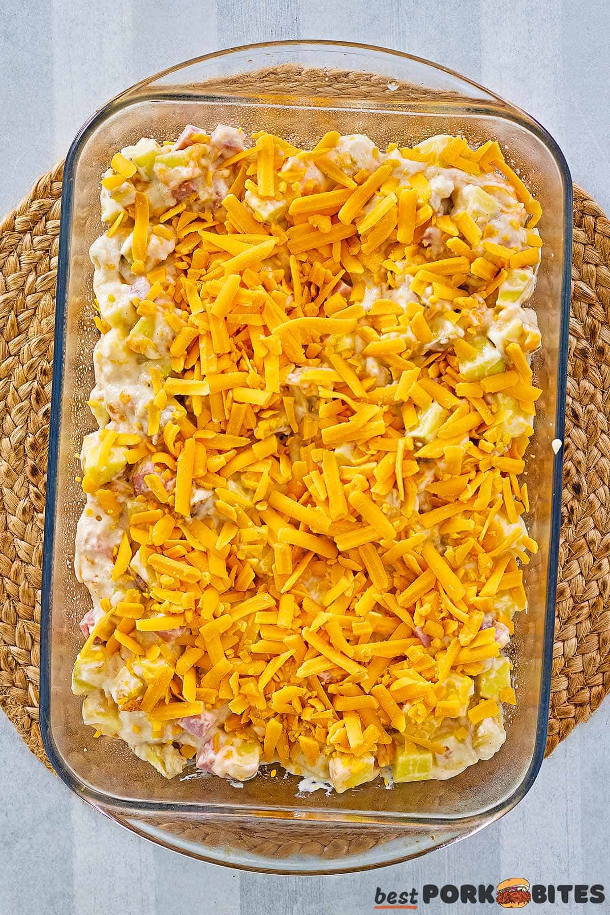 a baking dish filled with unbaked casserole topped with shredded cheddar