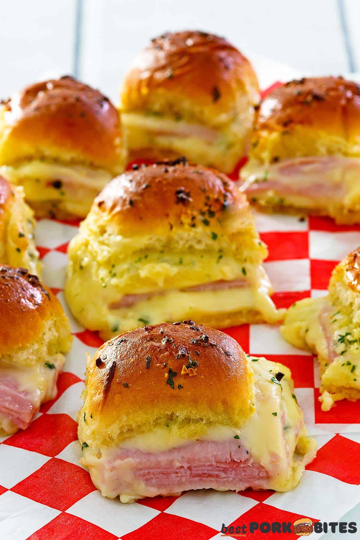 multiple baked ham and cheese sliders on checkered paper