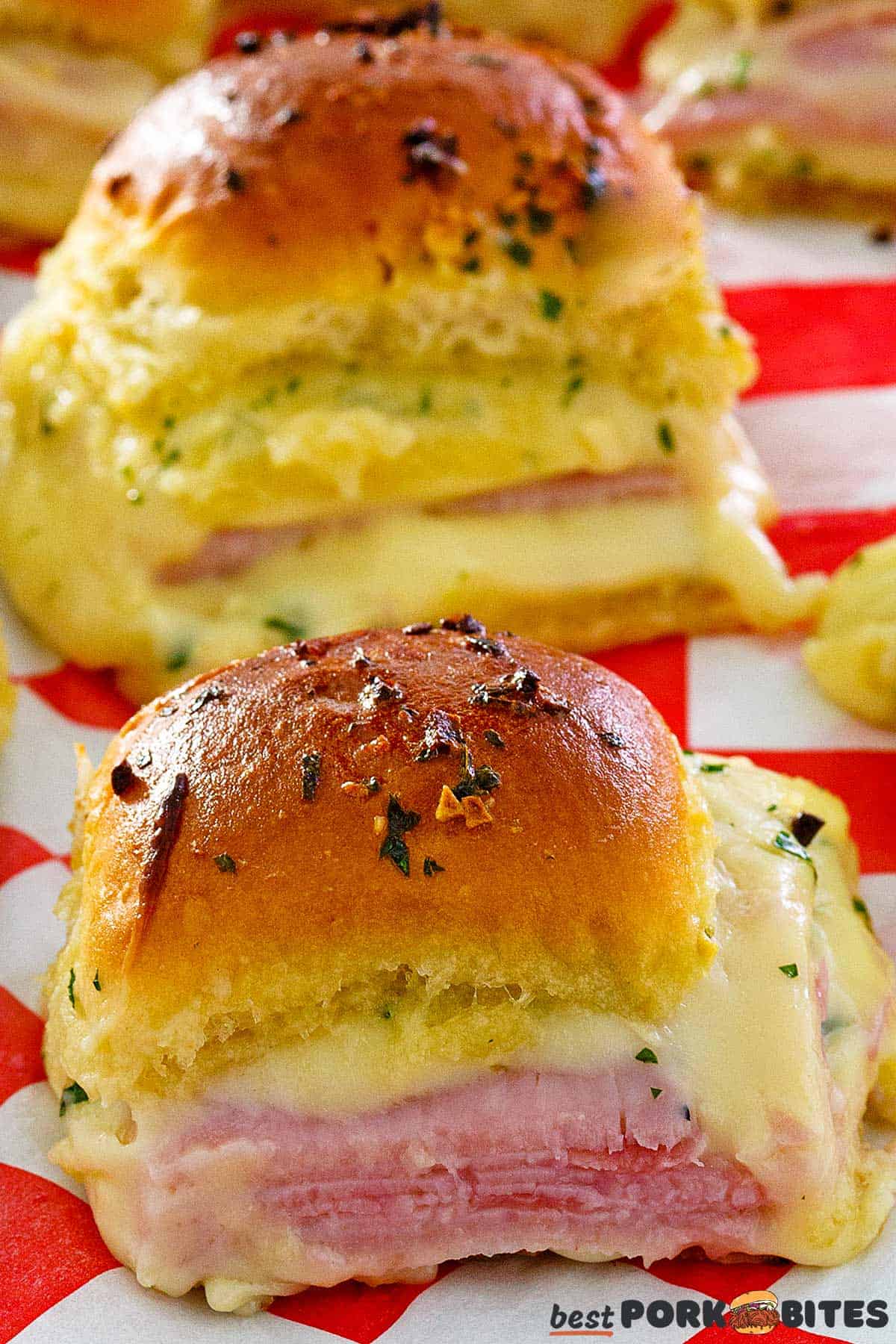 a closeup of two cooked ham and cheese sliders on checkered paper