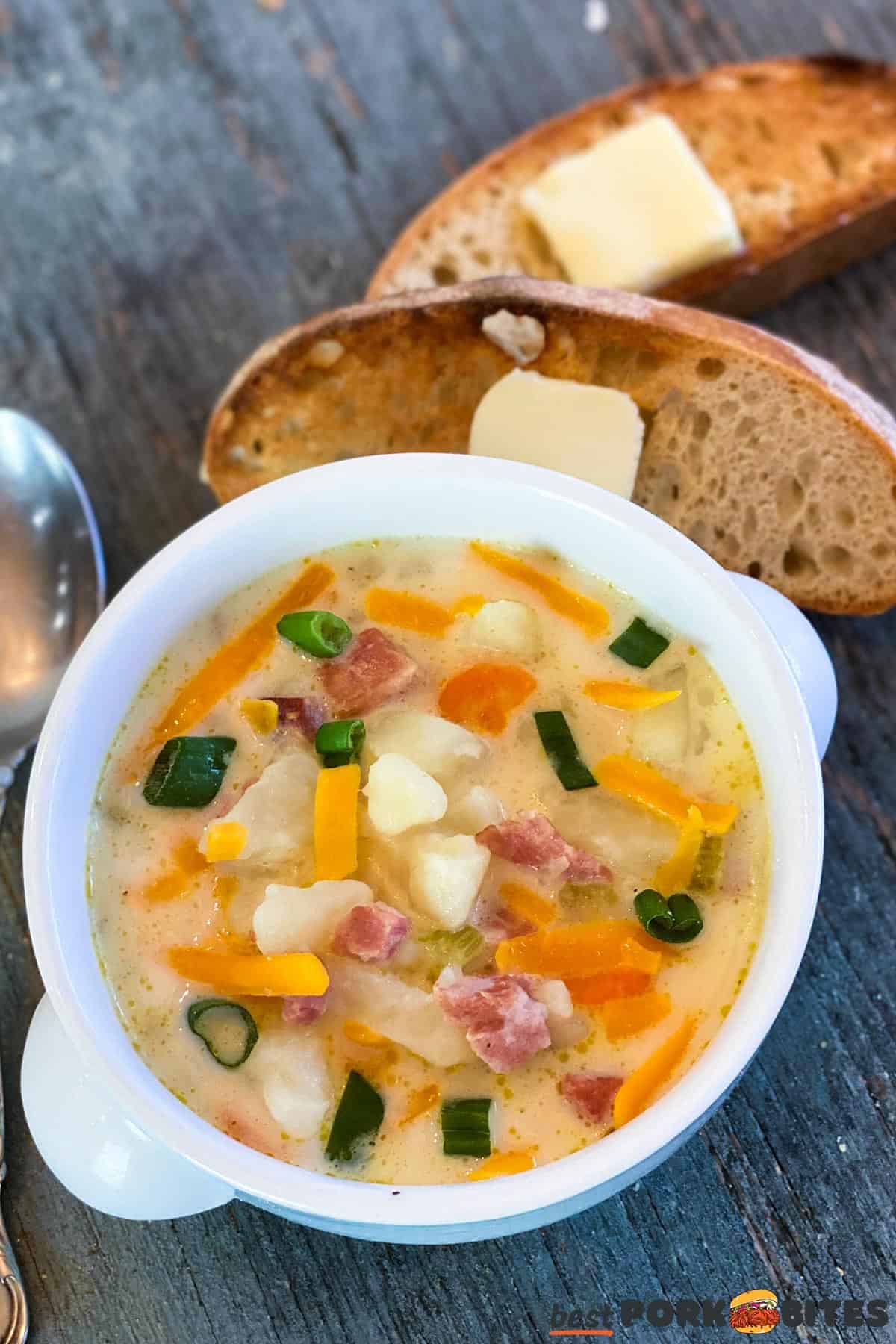 a bowl of ham and potato soup next to two slices of bread with butter