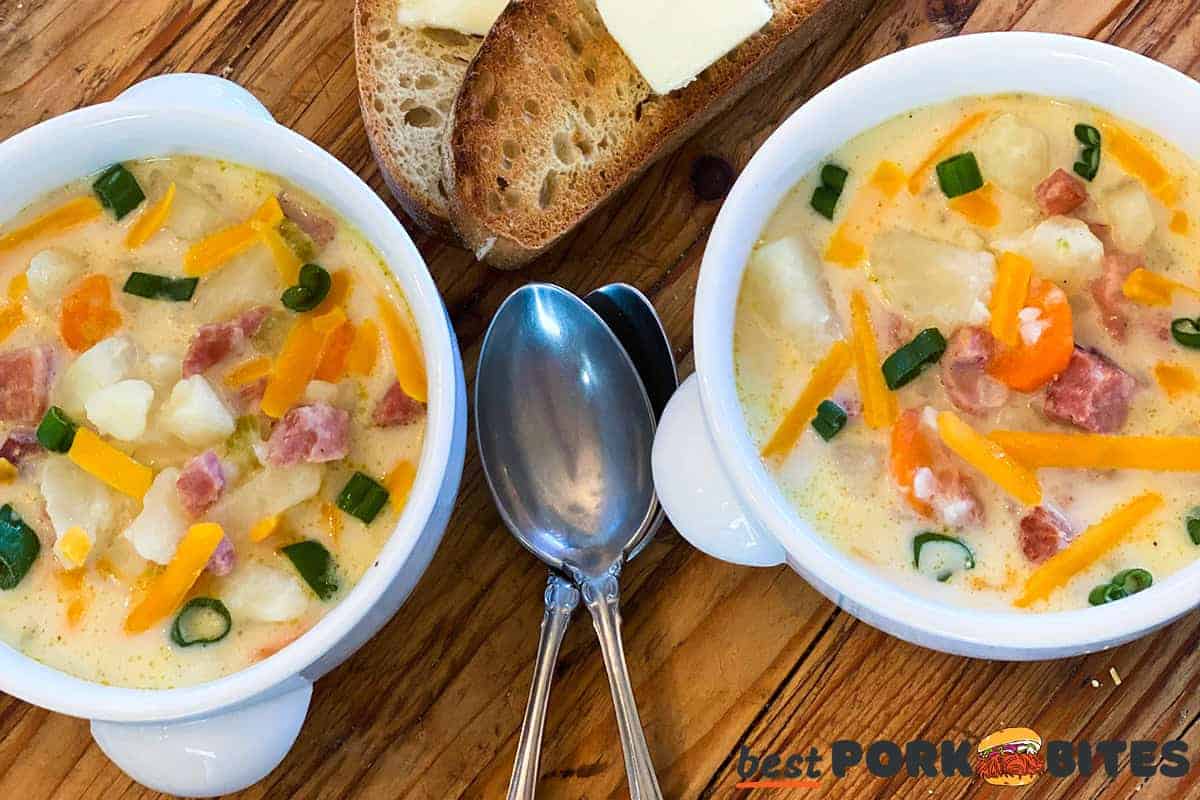 two bowls of completed ham and potato soup with spoons and bread