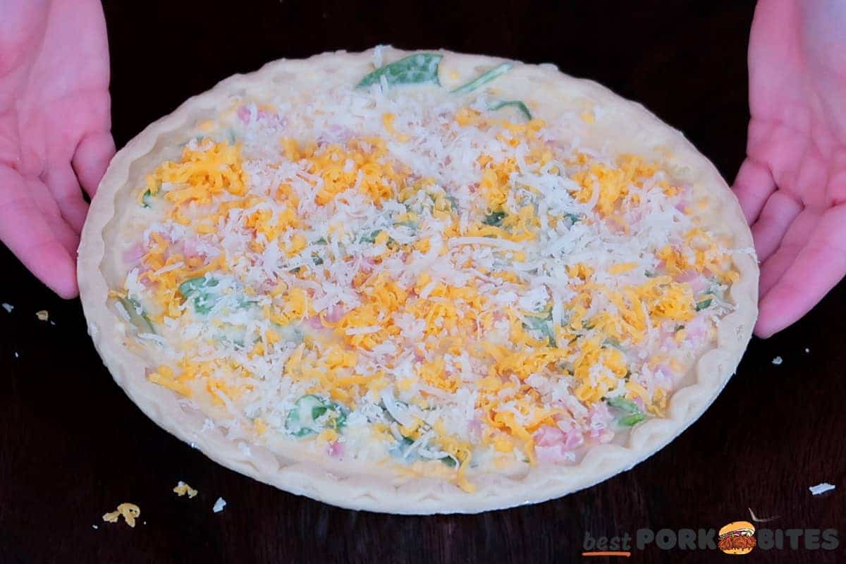ham quiche in a pie crust with shredded cheese on top