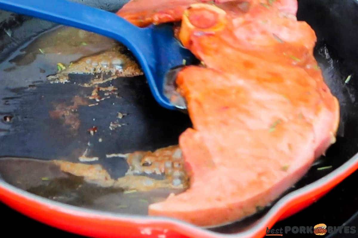 a fully cooked and glazed ham steak being scooped out of the skillet