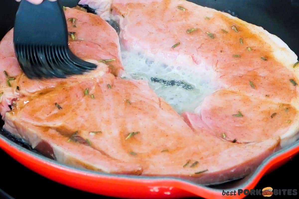 glaze being brushed on ham steaks in a skillet