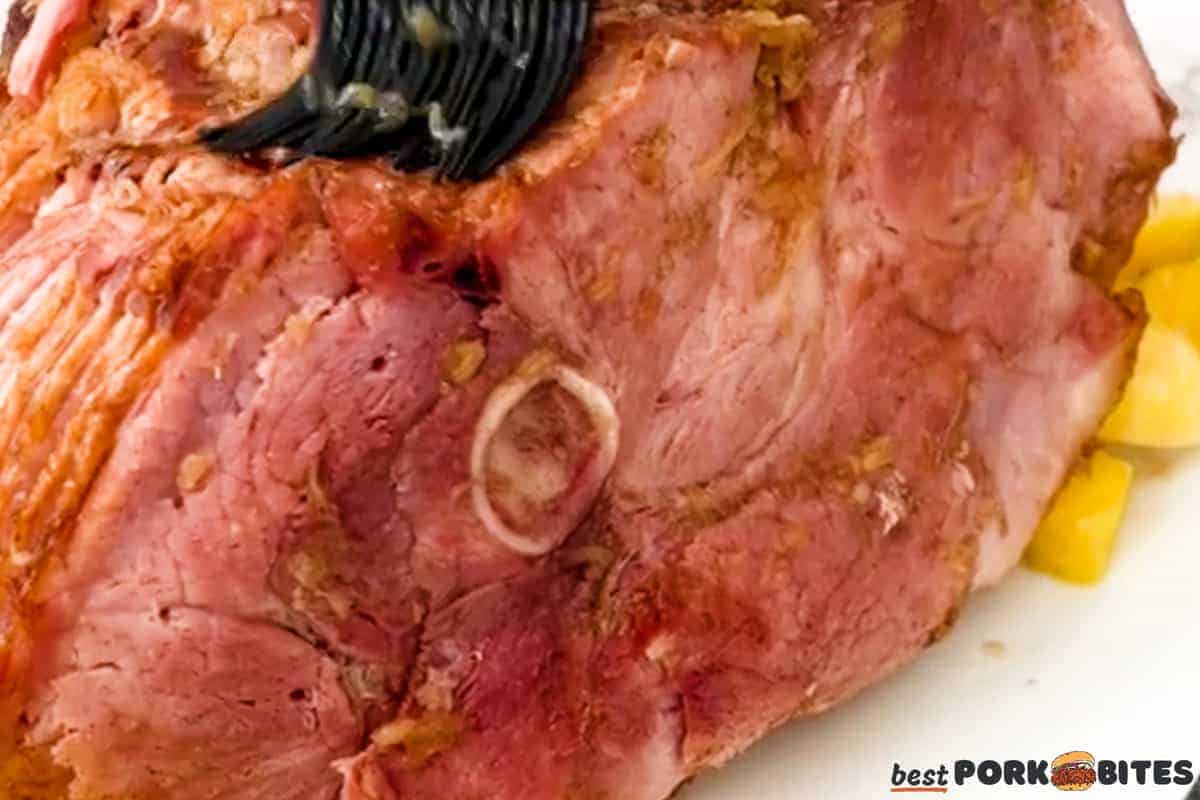 a closeup of a baked spiral ham being brushed with glaze
