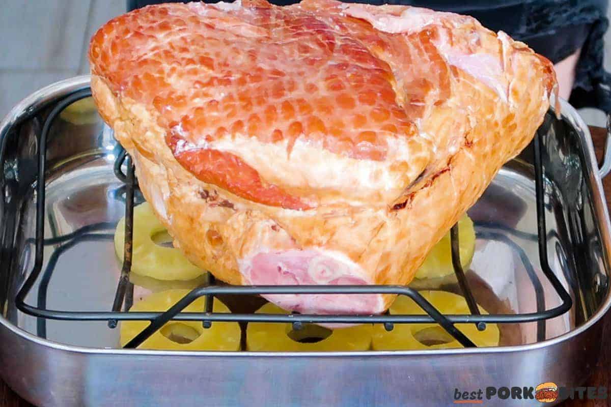 a ham on a baking rack in a dish filled with pineapple rings