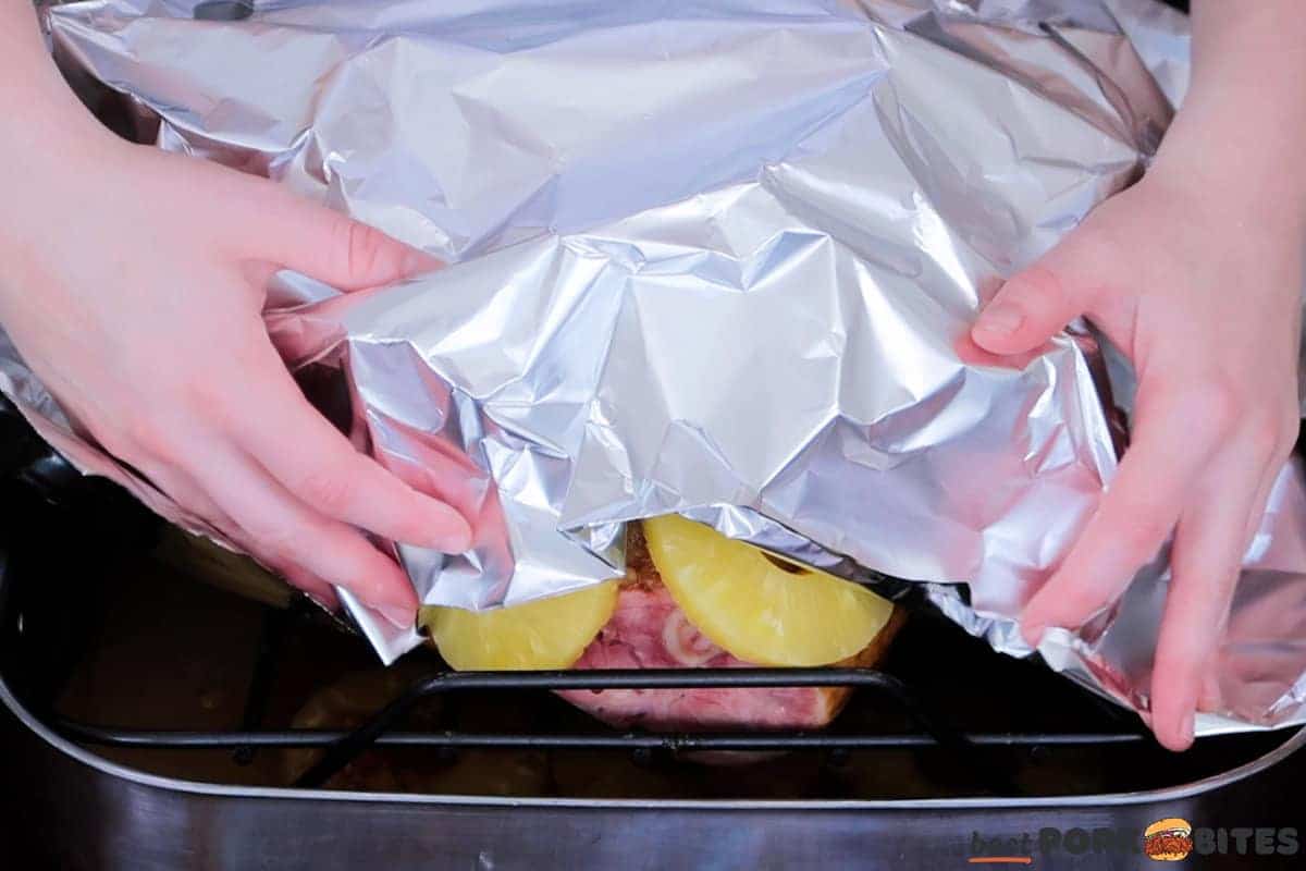 hands covering a pineapple ham with foil
