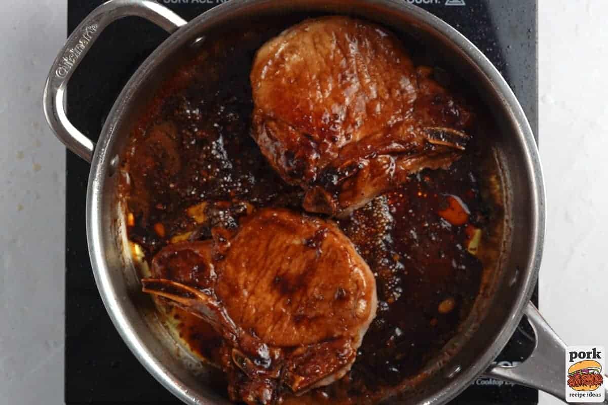 the pork chops simmering in a pan of glaze