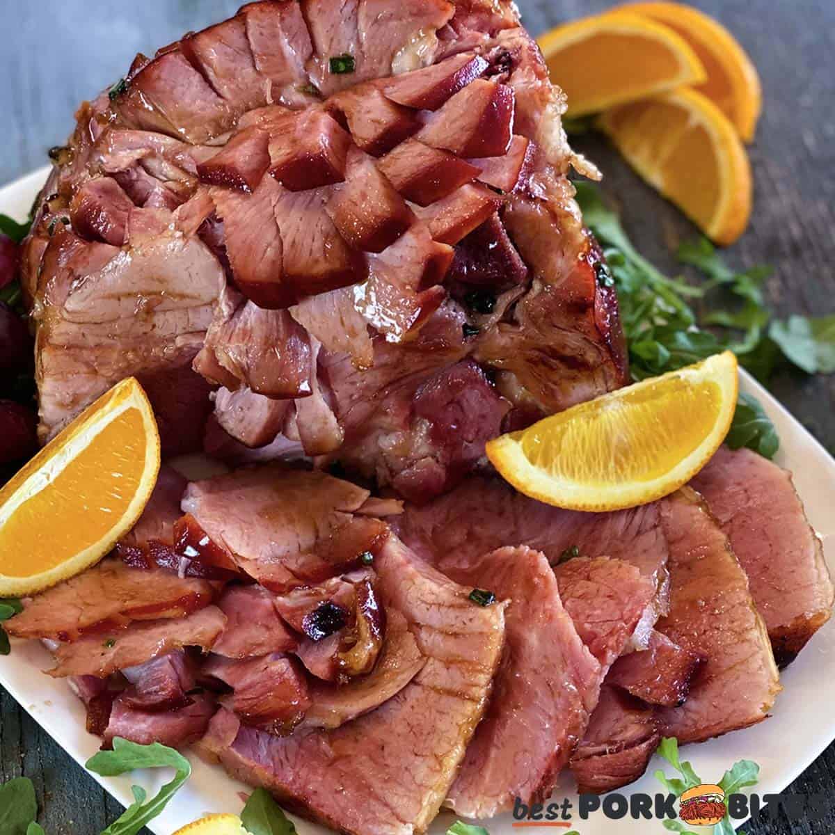 completed instant pot ham on a white plate with orange slices and arugula