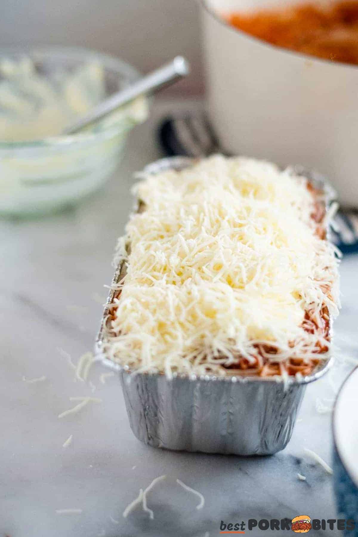 unbaked lasagna in a baking tin covered in mozzarella cheese with bowls in the background