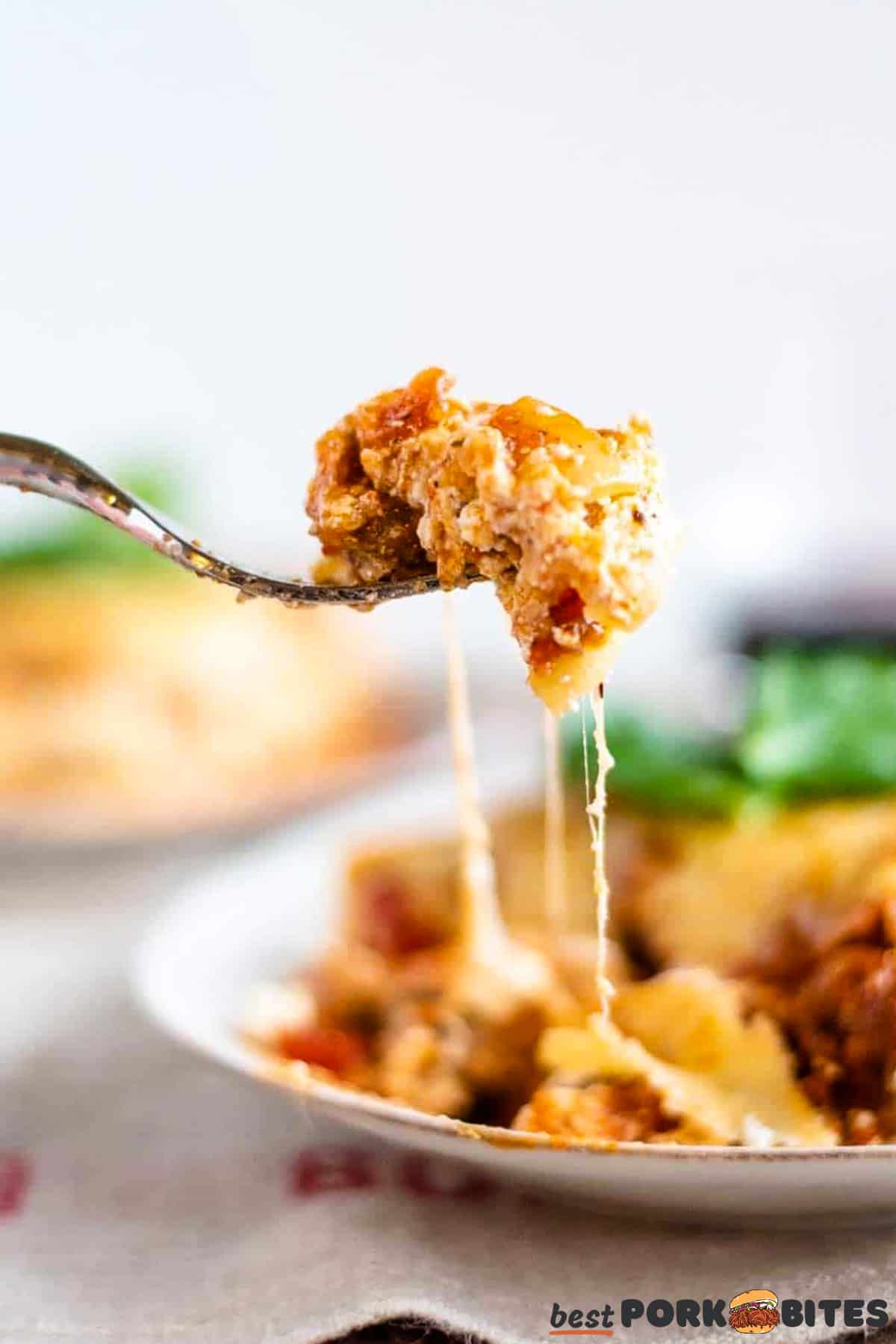 a fork lifting a bite of lasagna off a plate
