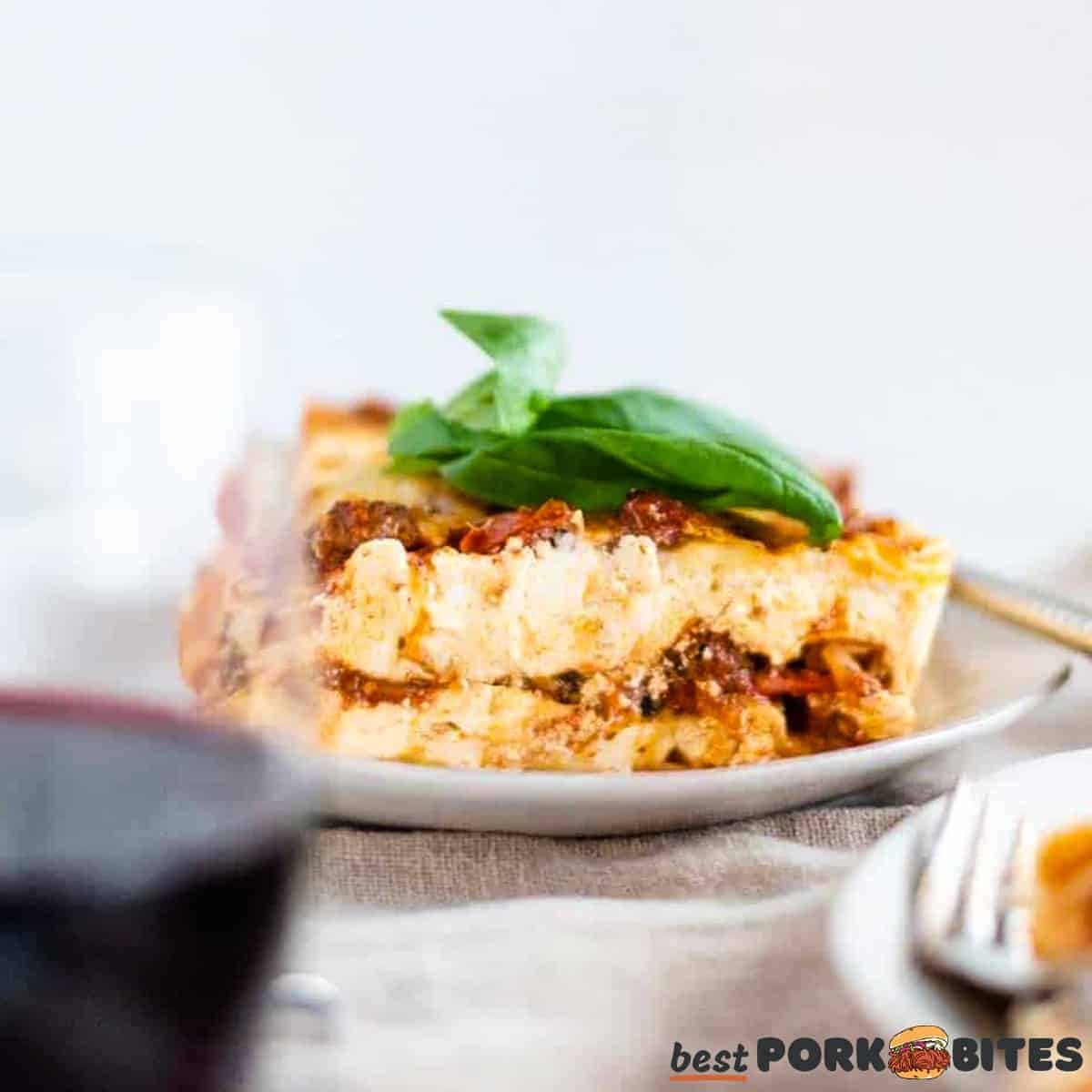 a white plate with a slice of lasagna on a towel with a plate and a glass of wine in front