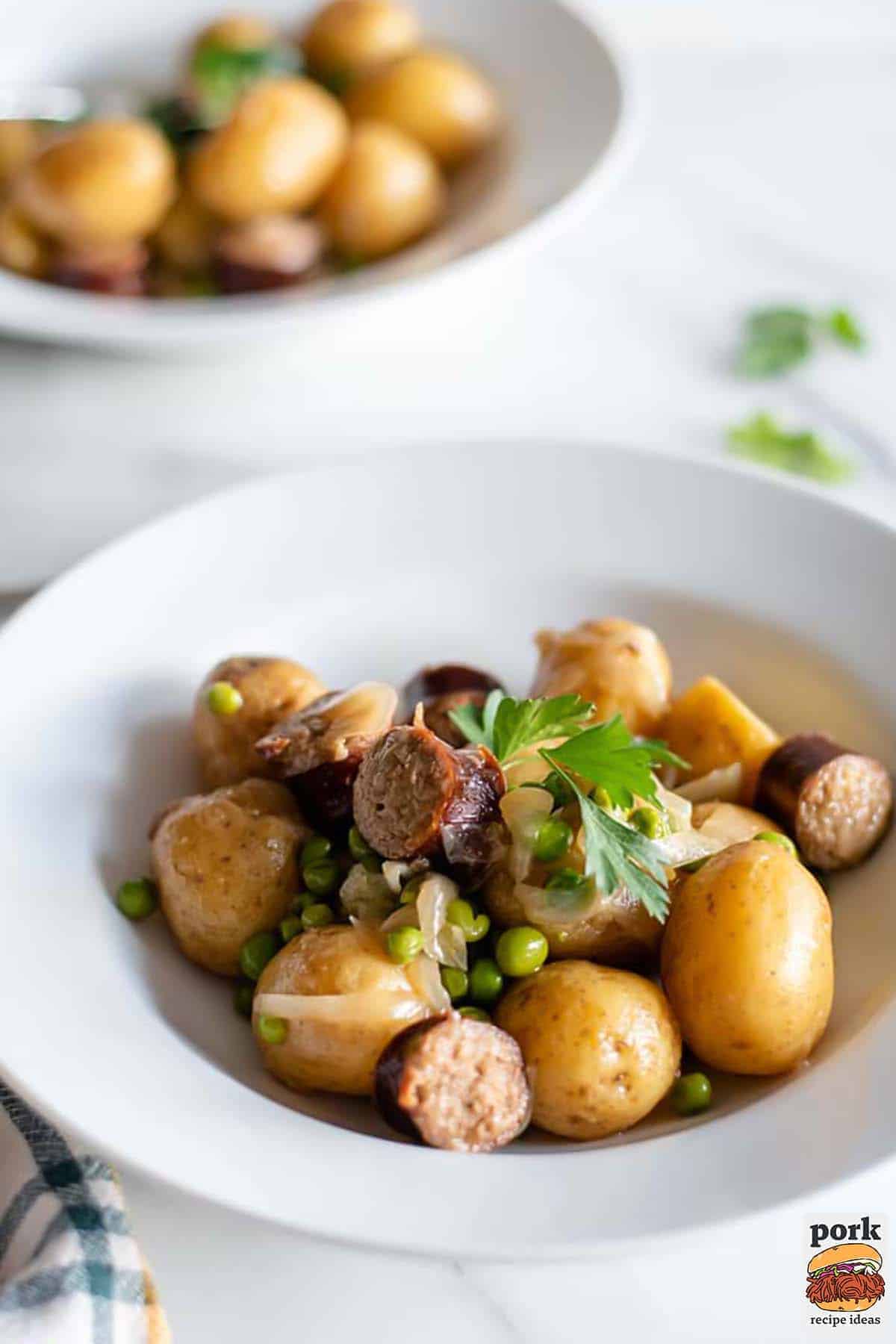 kielbasa and potatoes on a white plate with parsley and peas