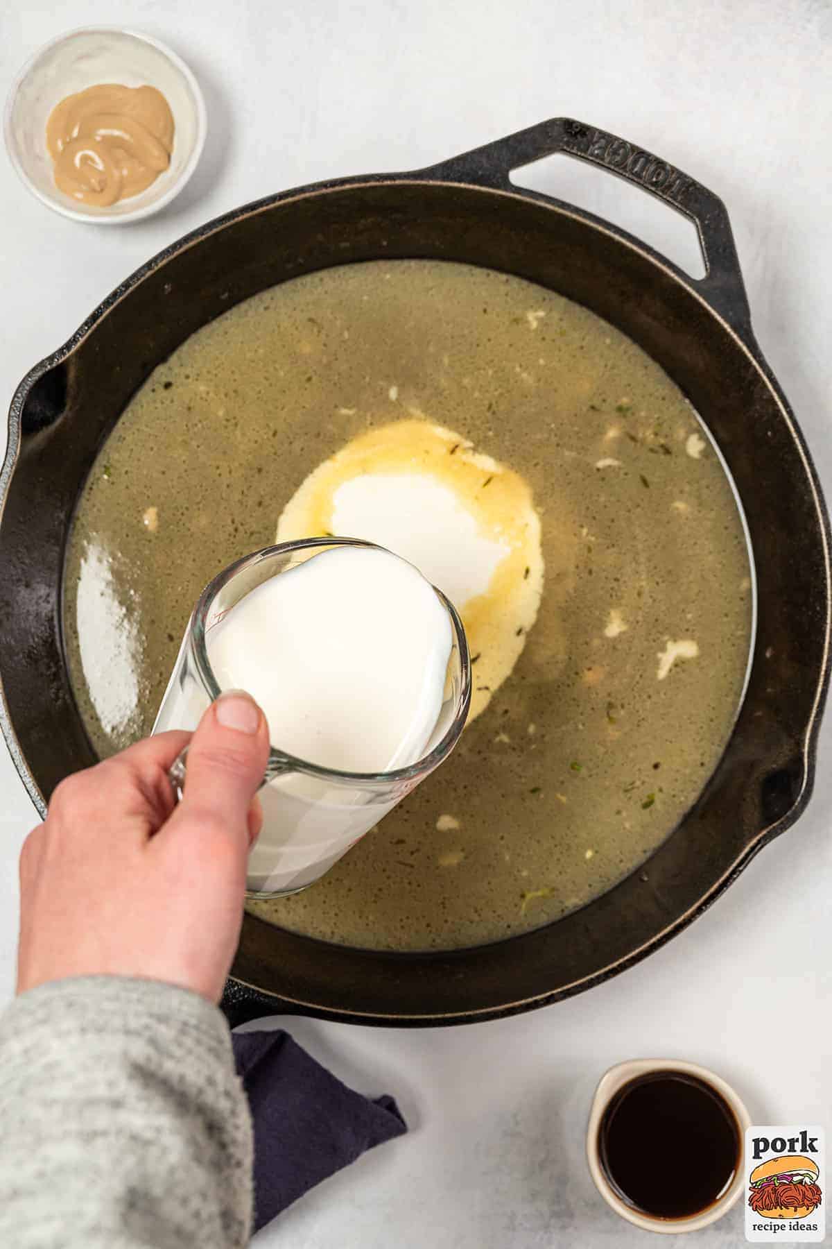 the cream being poured into the pan of chicken stock and drippings