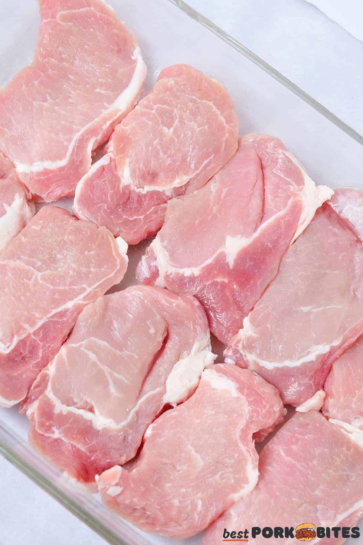 raw pork chops lined up in a glass dish