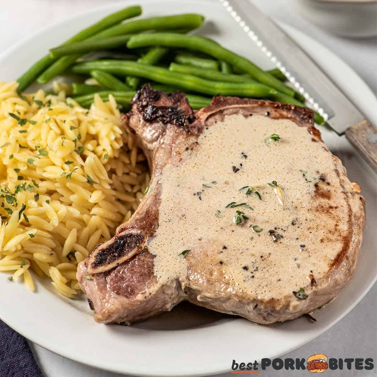 pan fried pork chop on a plate with orzo and green beans