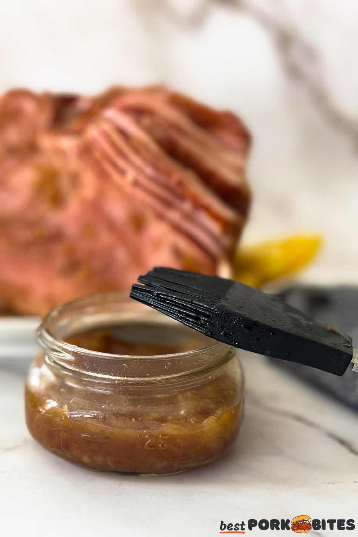 a jar of pineapple ham glaze with a basting brush in front of a glazed spiral cut ham