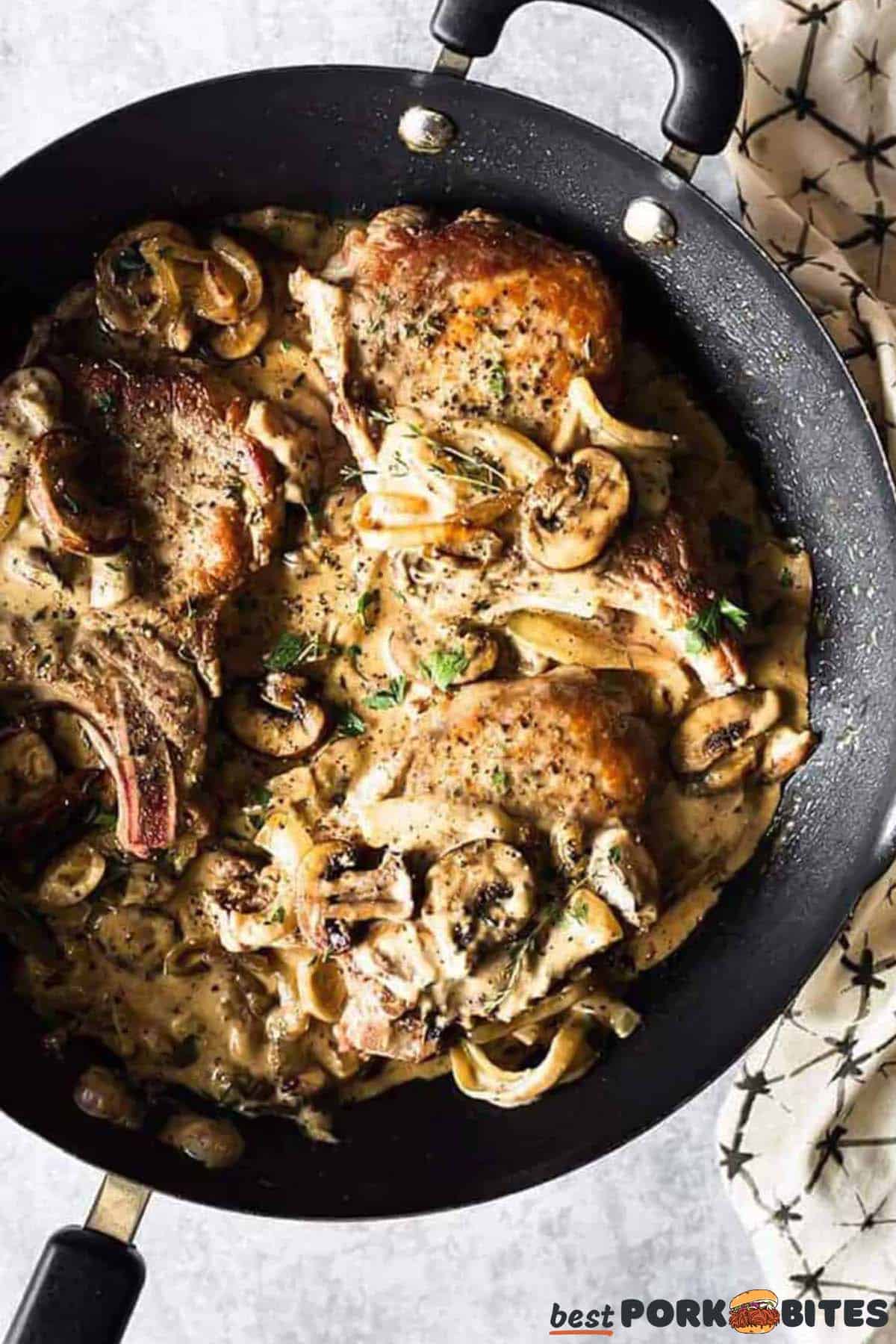 pork chops smothered with mushrooms in a black skillet with herbs