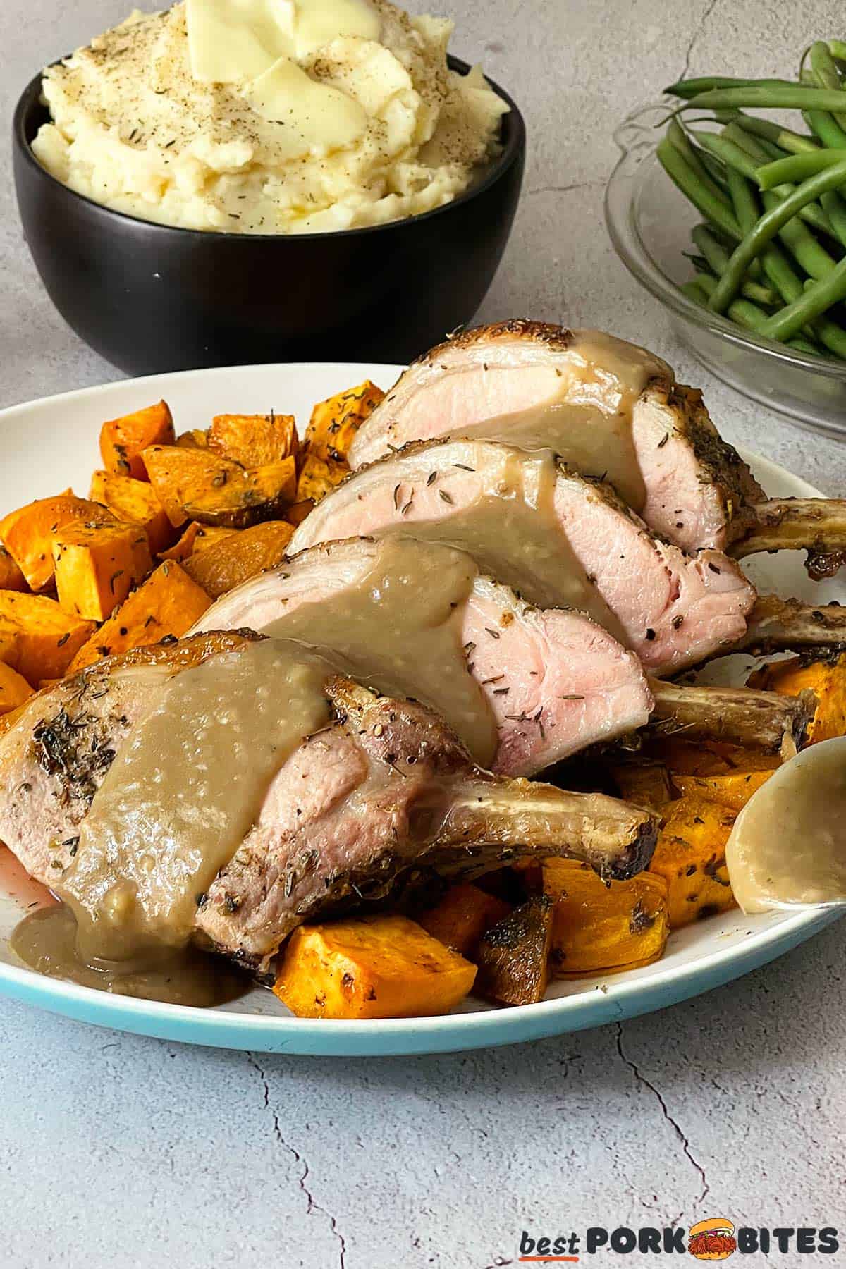 pork rib roast sliced with gravy over top on a white plate with sweet potatoes