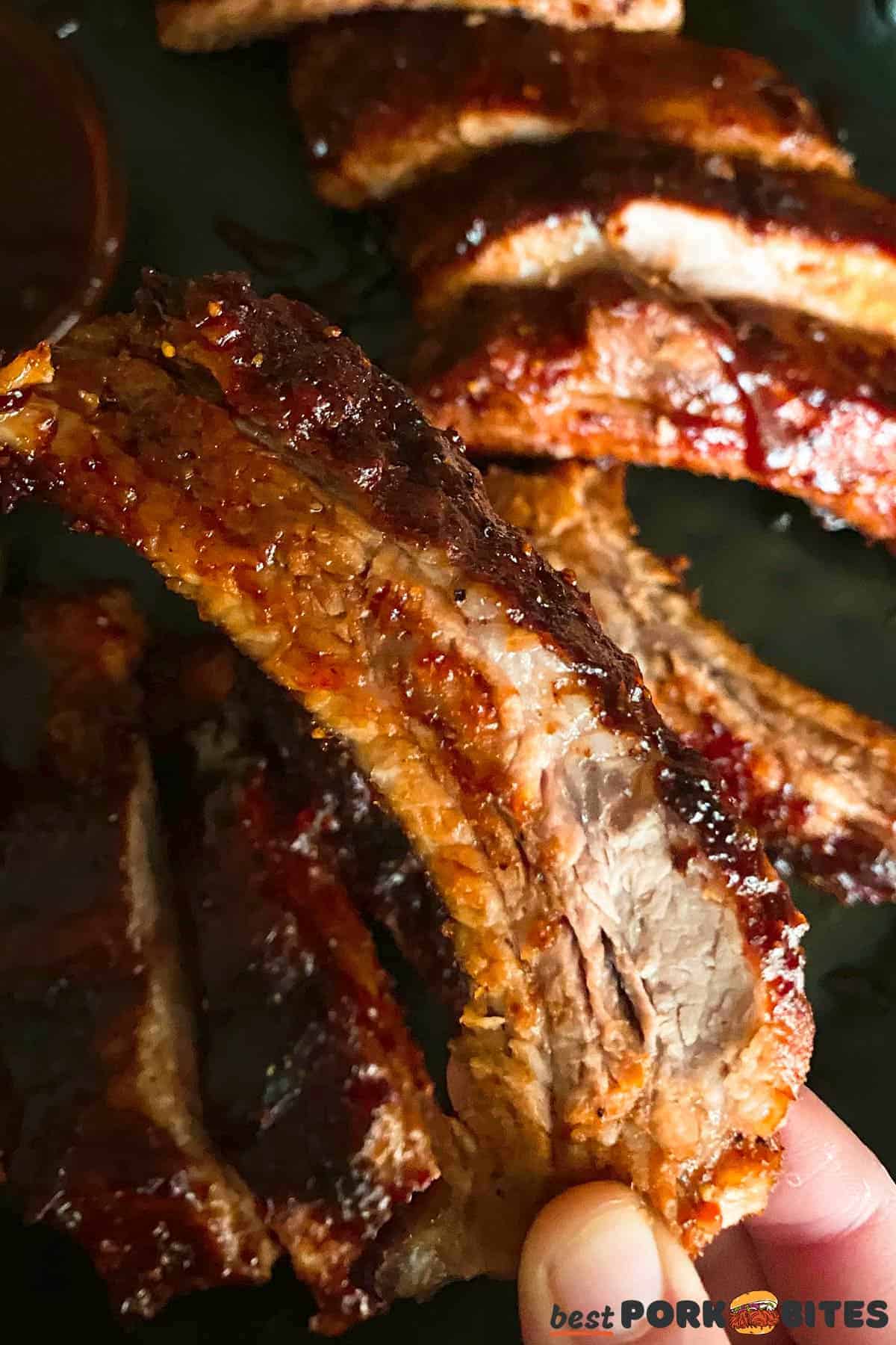 fingers holding up a cooked pork rib with BBQ sauce