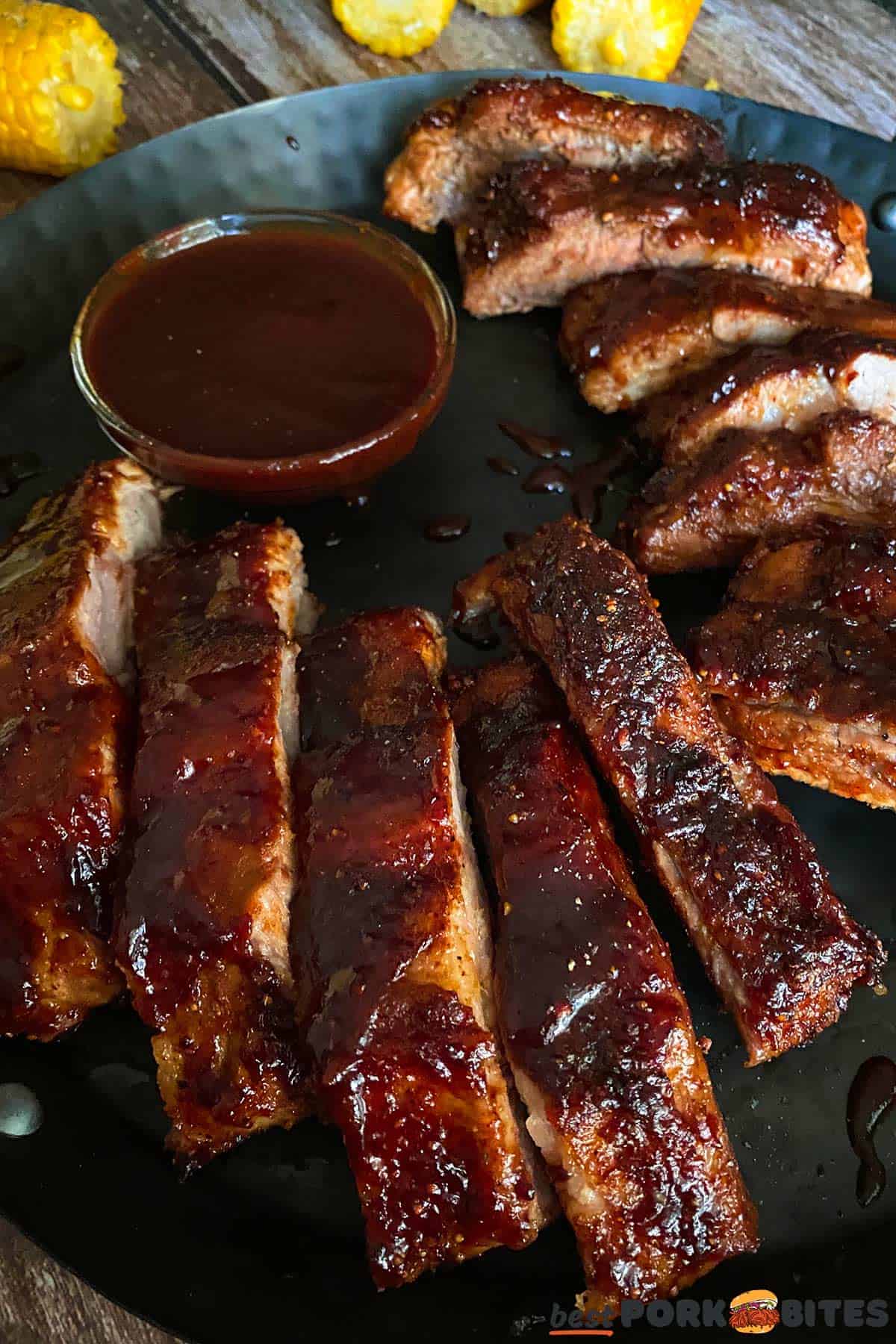 a black platter with pork ribs and extra sauce