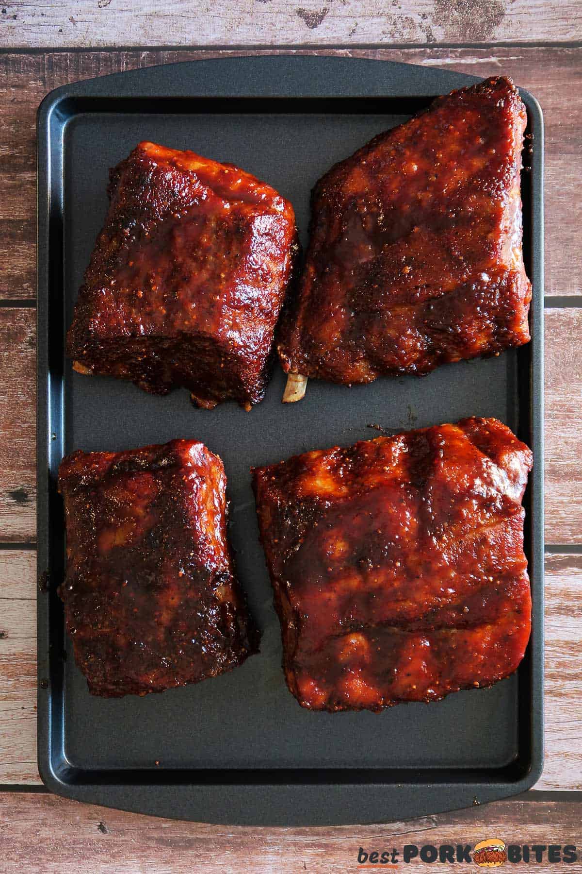 four slices of ribs covered in BBQ sauce on a baking tray