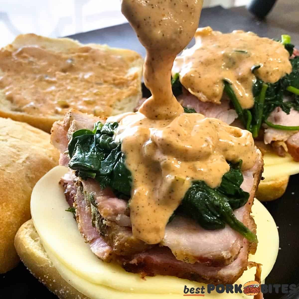 a roast pork sandwich with remoulade being poured on with a spoon