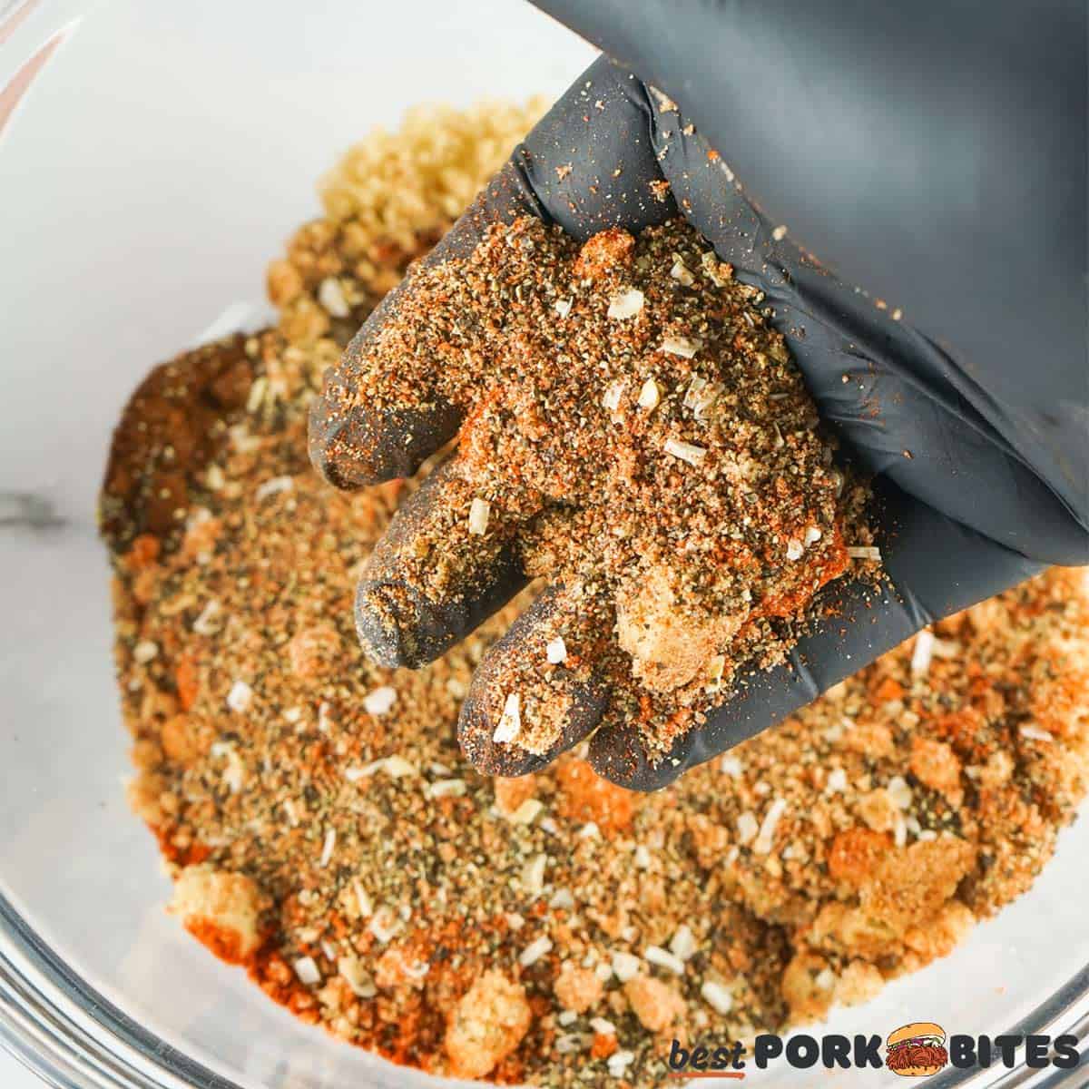 lifting pork rub out of a bowl with gloved hand