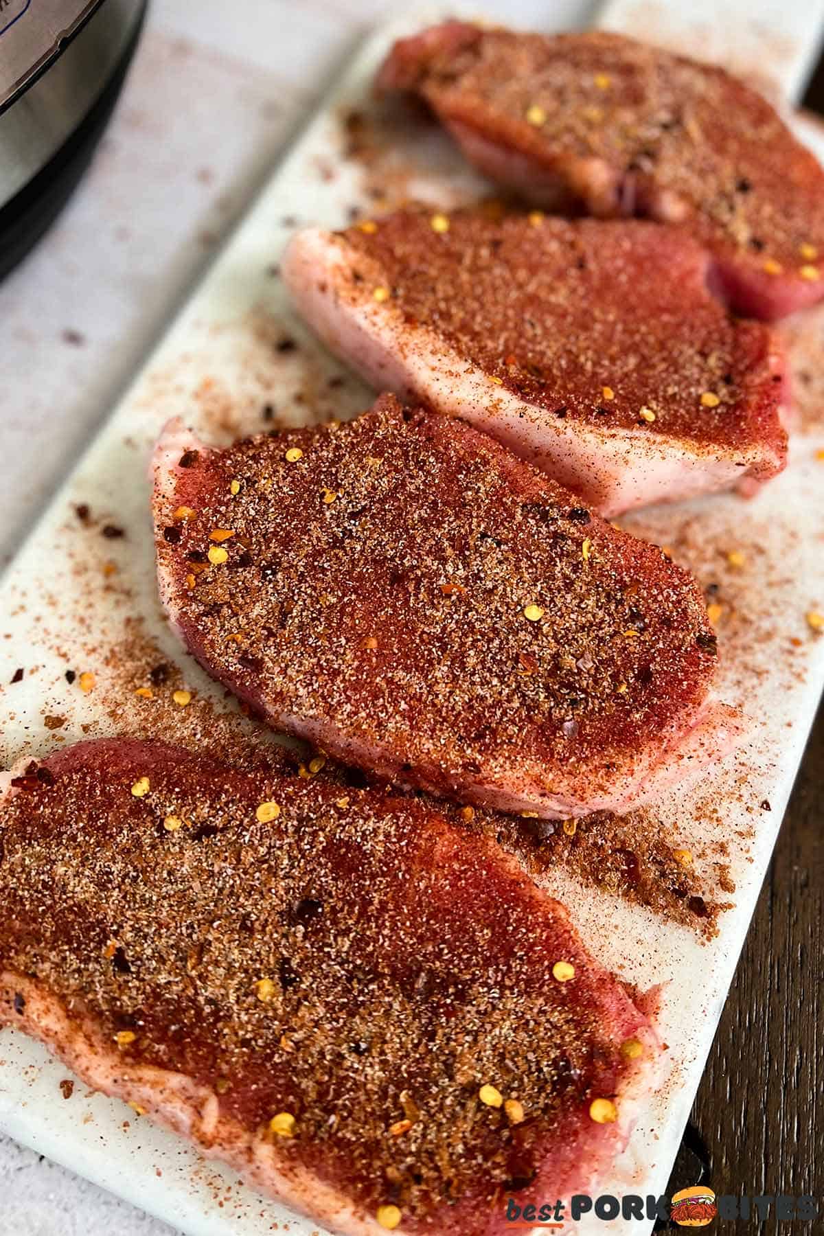 raw, seasoned pork chops on a cutting board