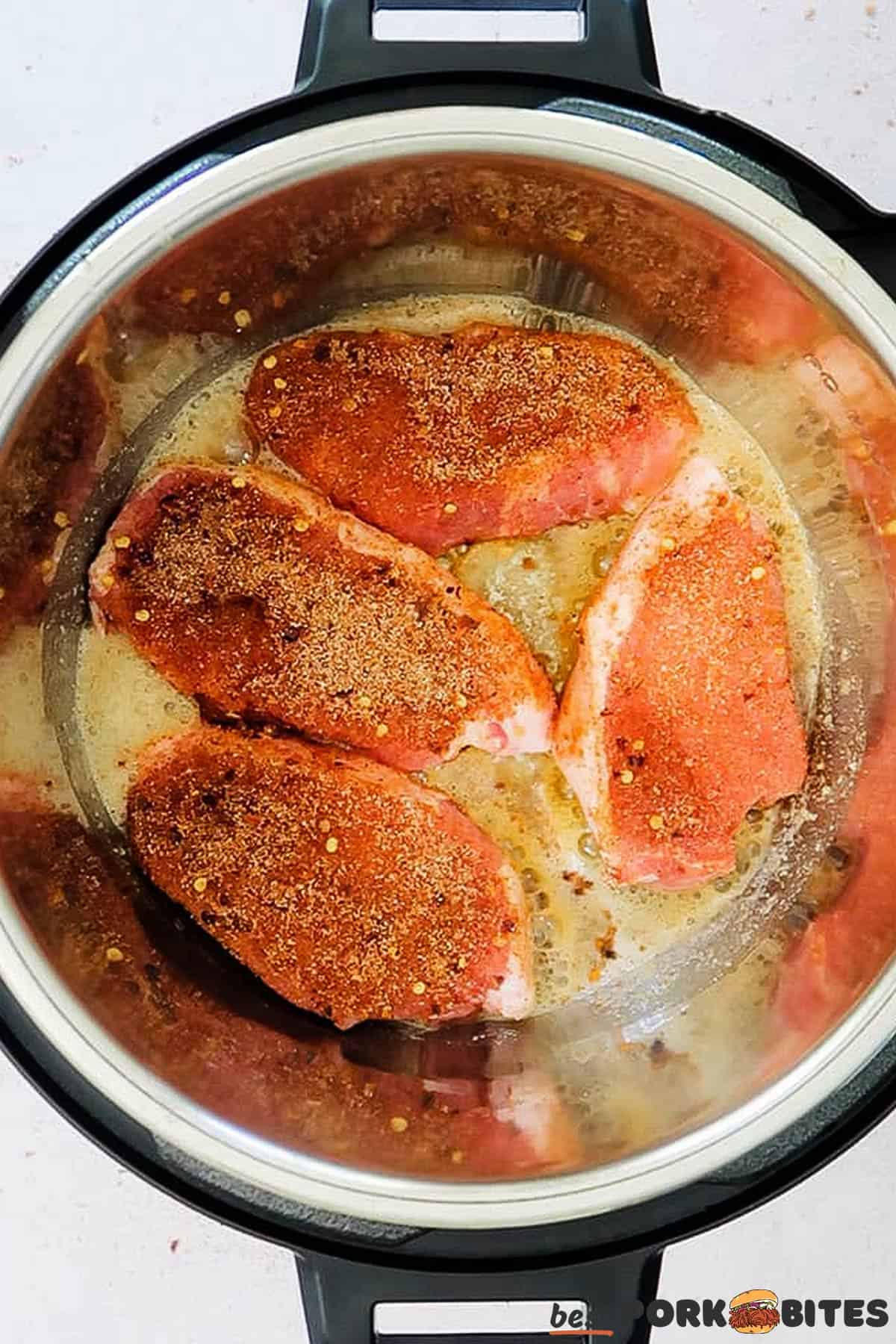 raw pork chops with seasoning in the pan of a pressure cooker filled with melted butter