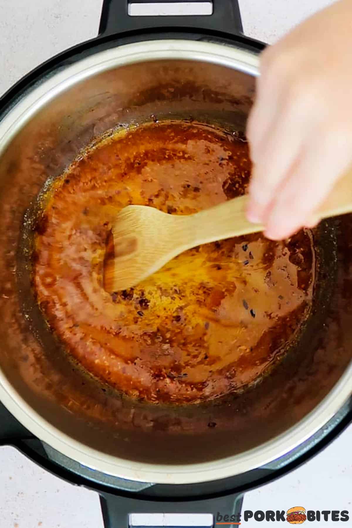 pork gravy being stirred in a pressure cooker with a wooden spatula