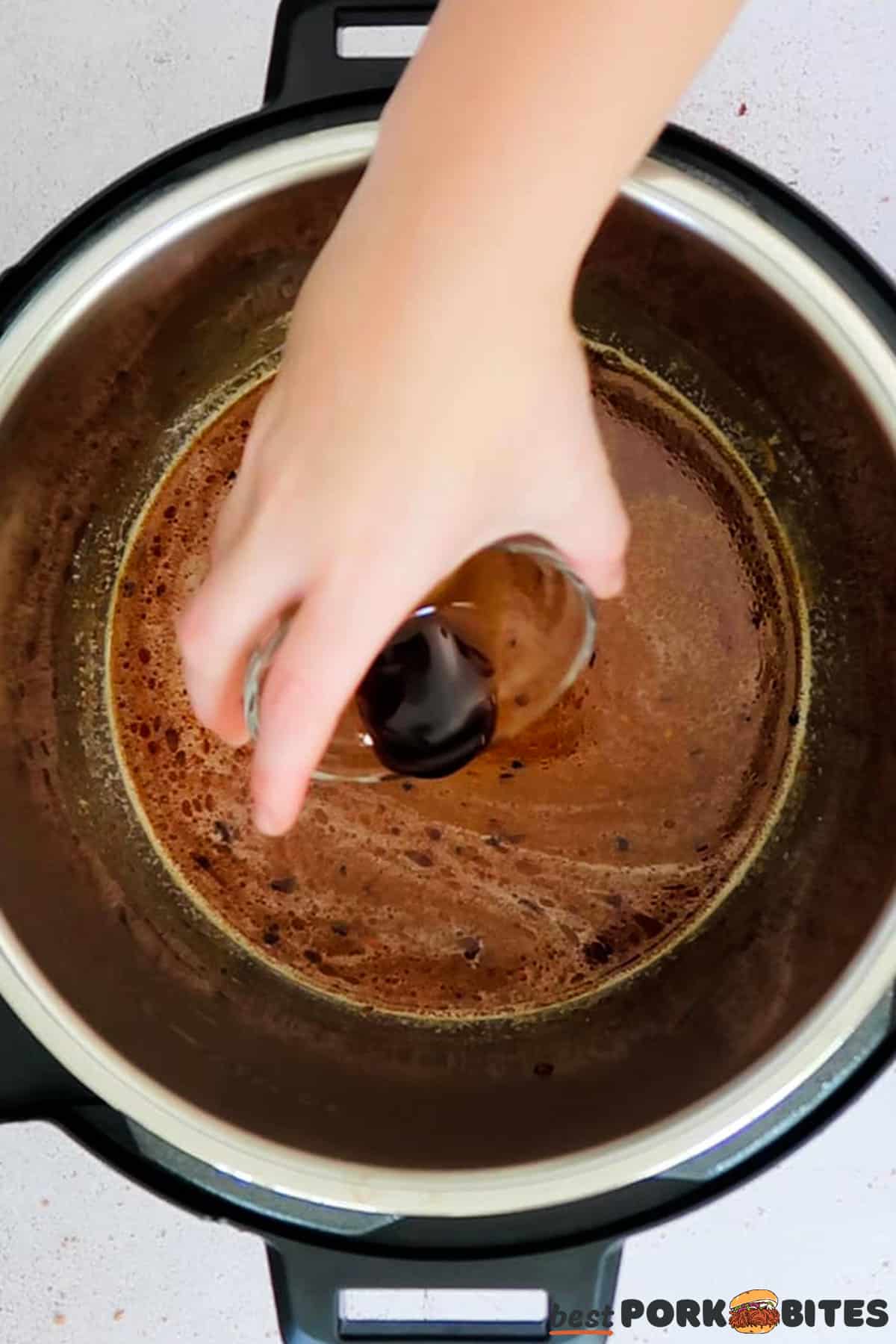 worcestershire sauce being poured into the pan of a pressure cooker filled with gravy