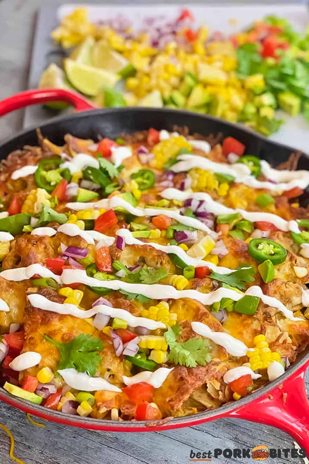 a red skillet with completed nachos in front of a cutting board filled with nacho toppings