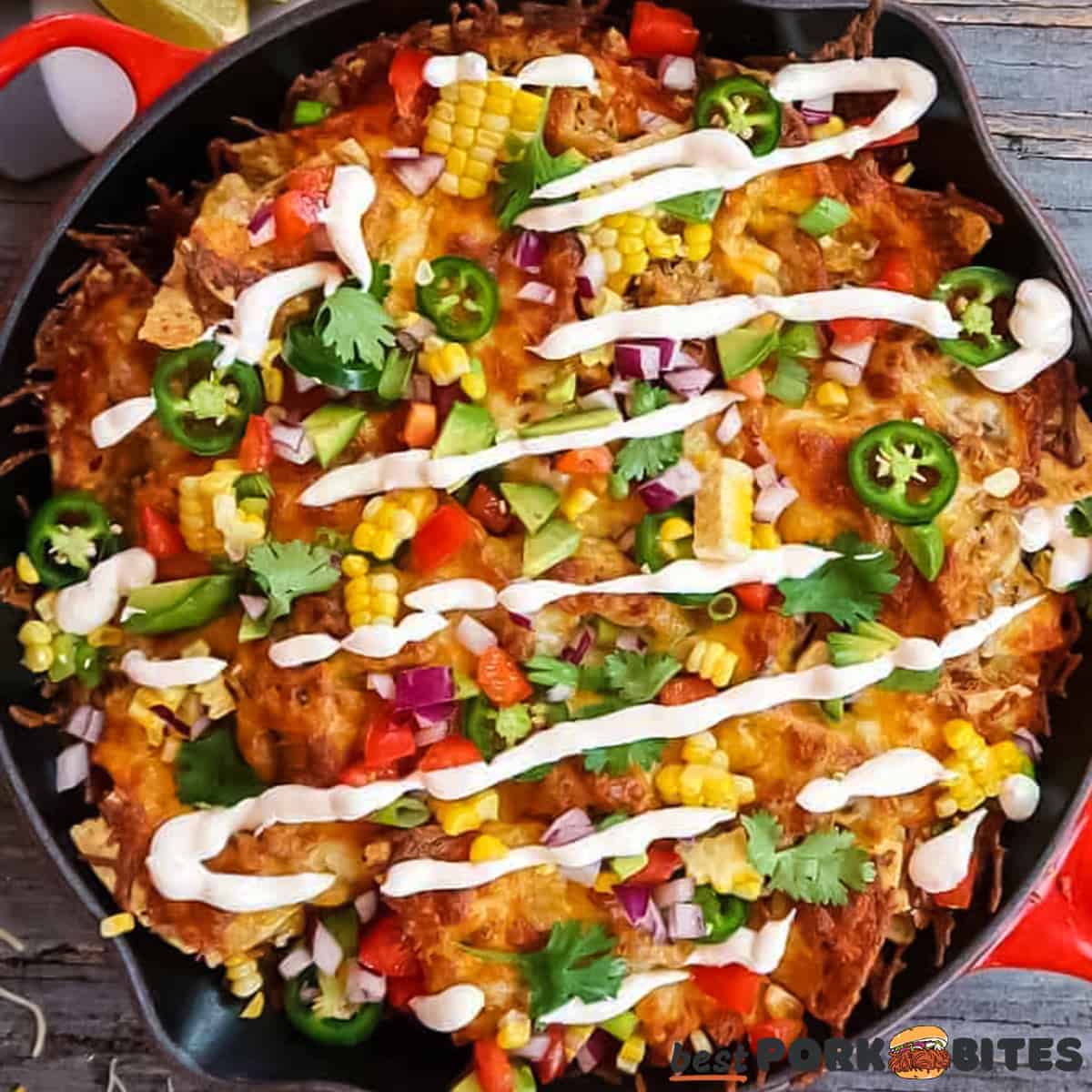 a skillet filled with completed and topped pulled pork nachos with sour cream drizzle