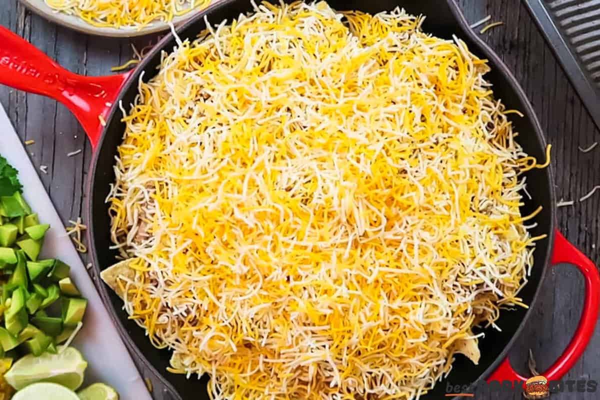 a pan of nachos covered in shredded cheese next to a cutting board with toppings