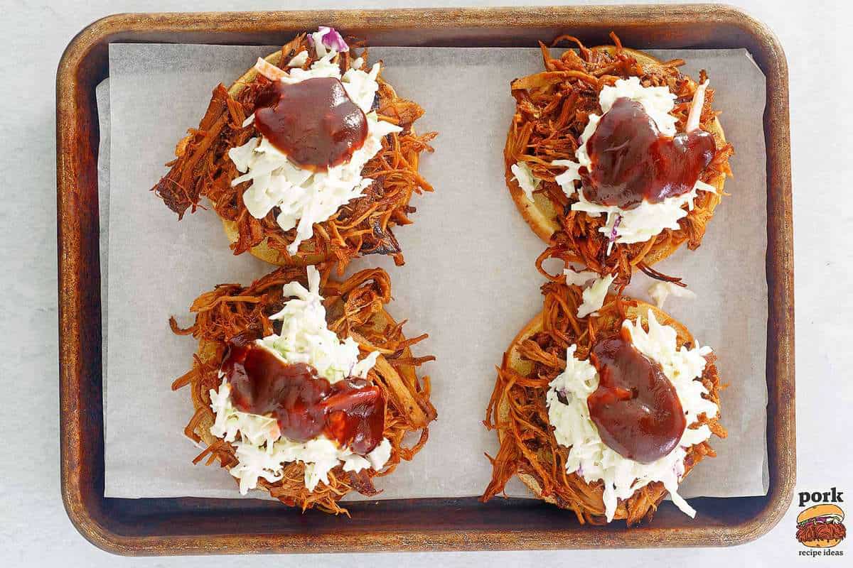 pulled pork sandwiches being assembled on a baking sheet with coleslaw and bbq