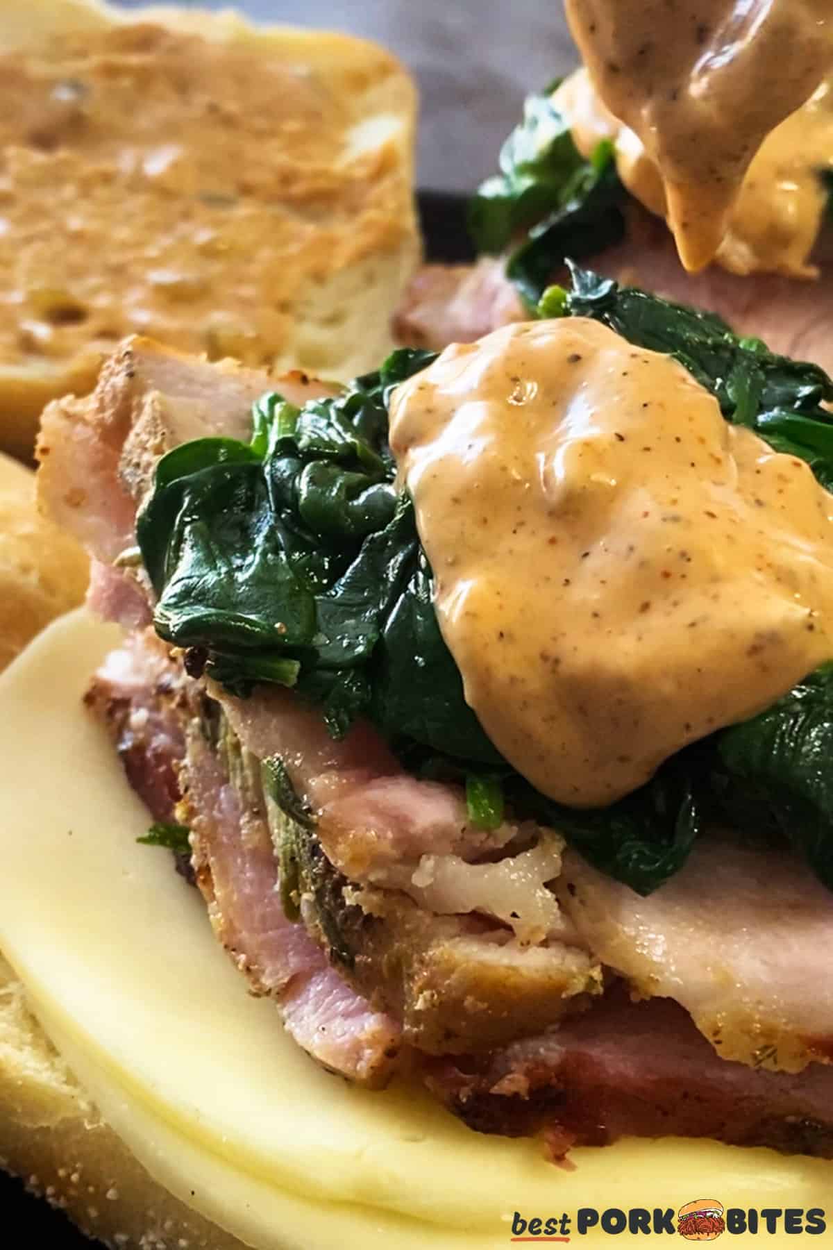 an open face roast pork sandwich with remoulade being added with a spoon