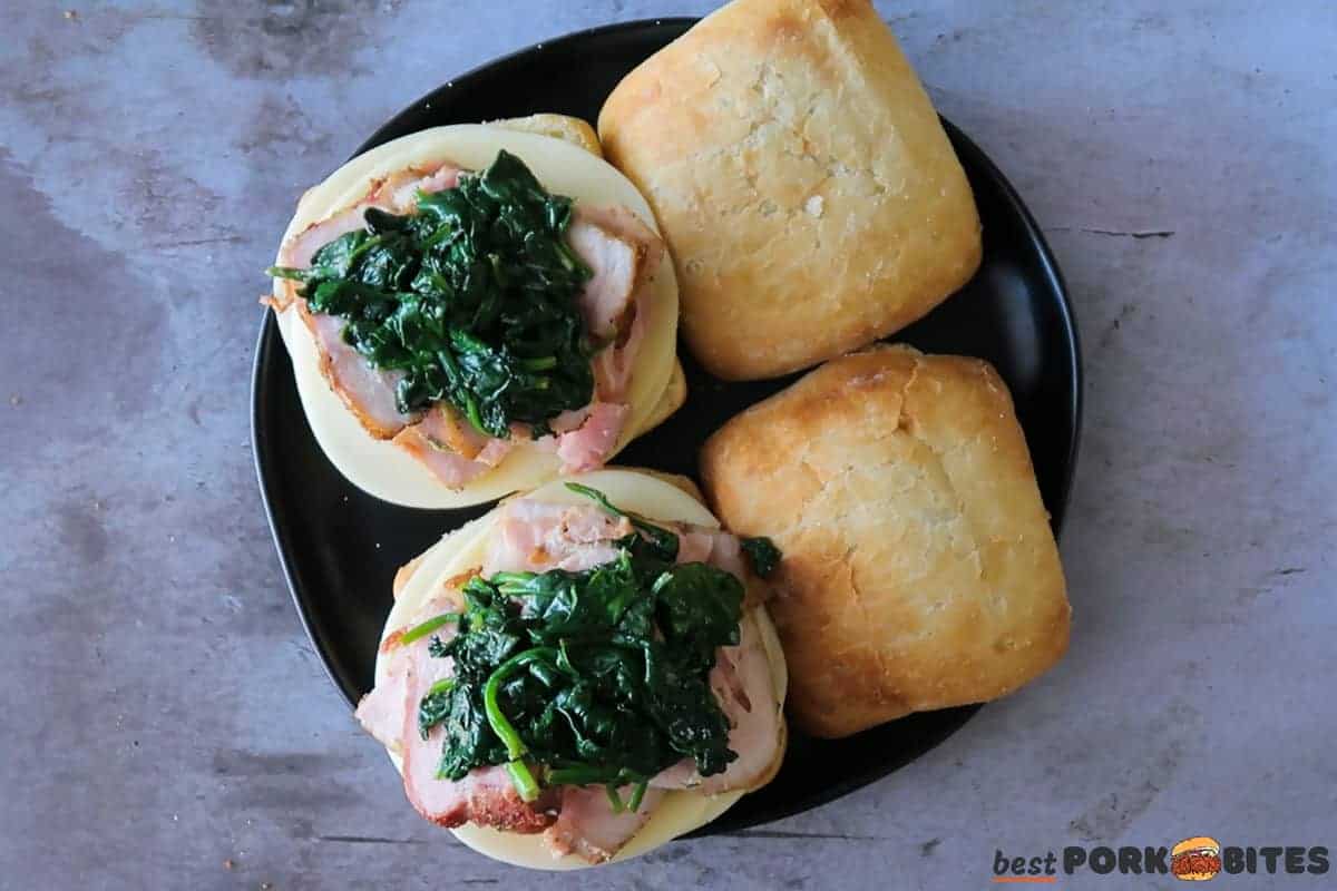 two roast pork sandwiches on a black plate with cheese, ham, and spinach