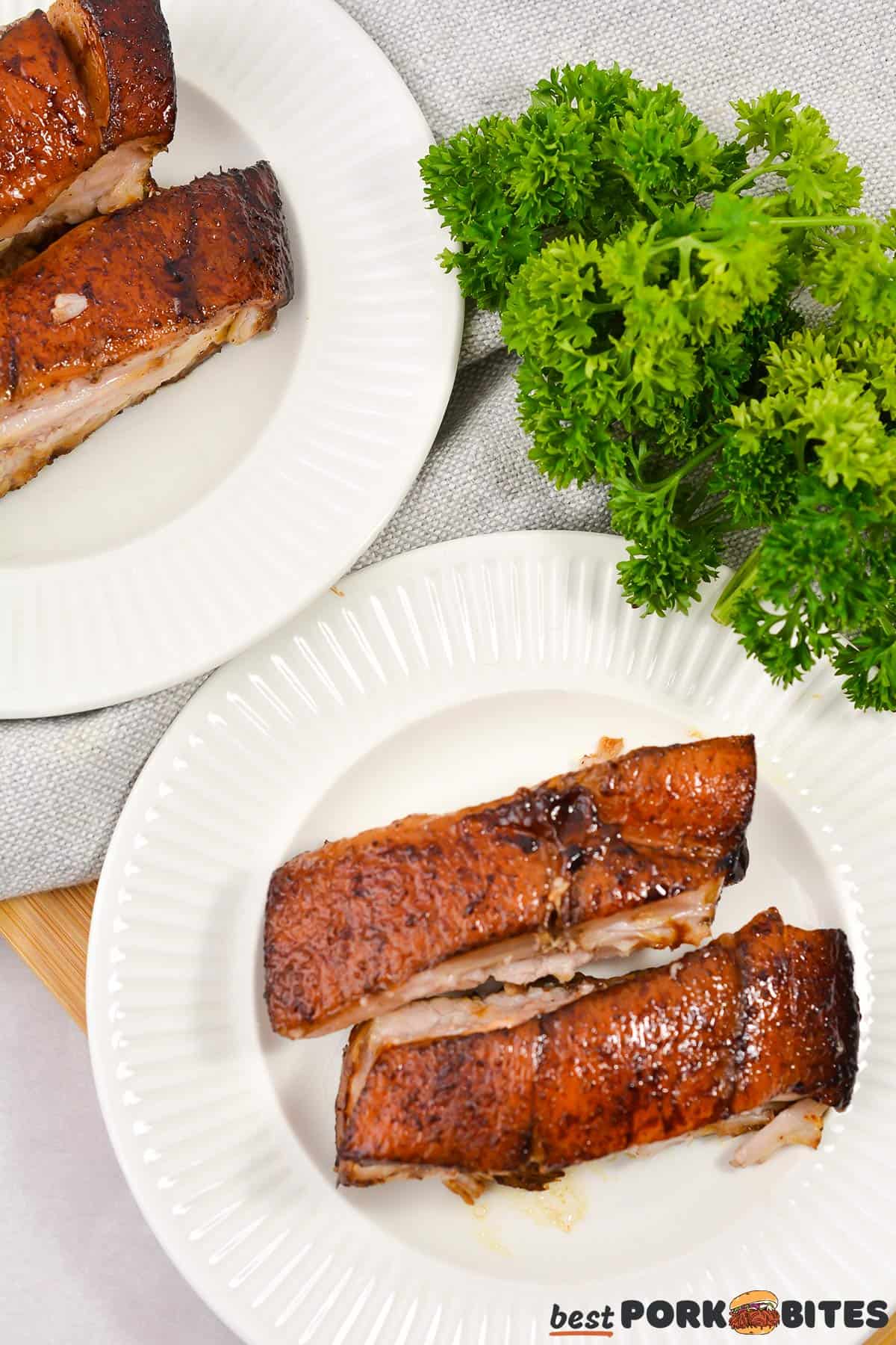 two white plates with two slices of pork belly each and a sprig of parsley
