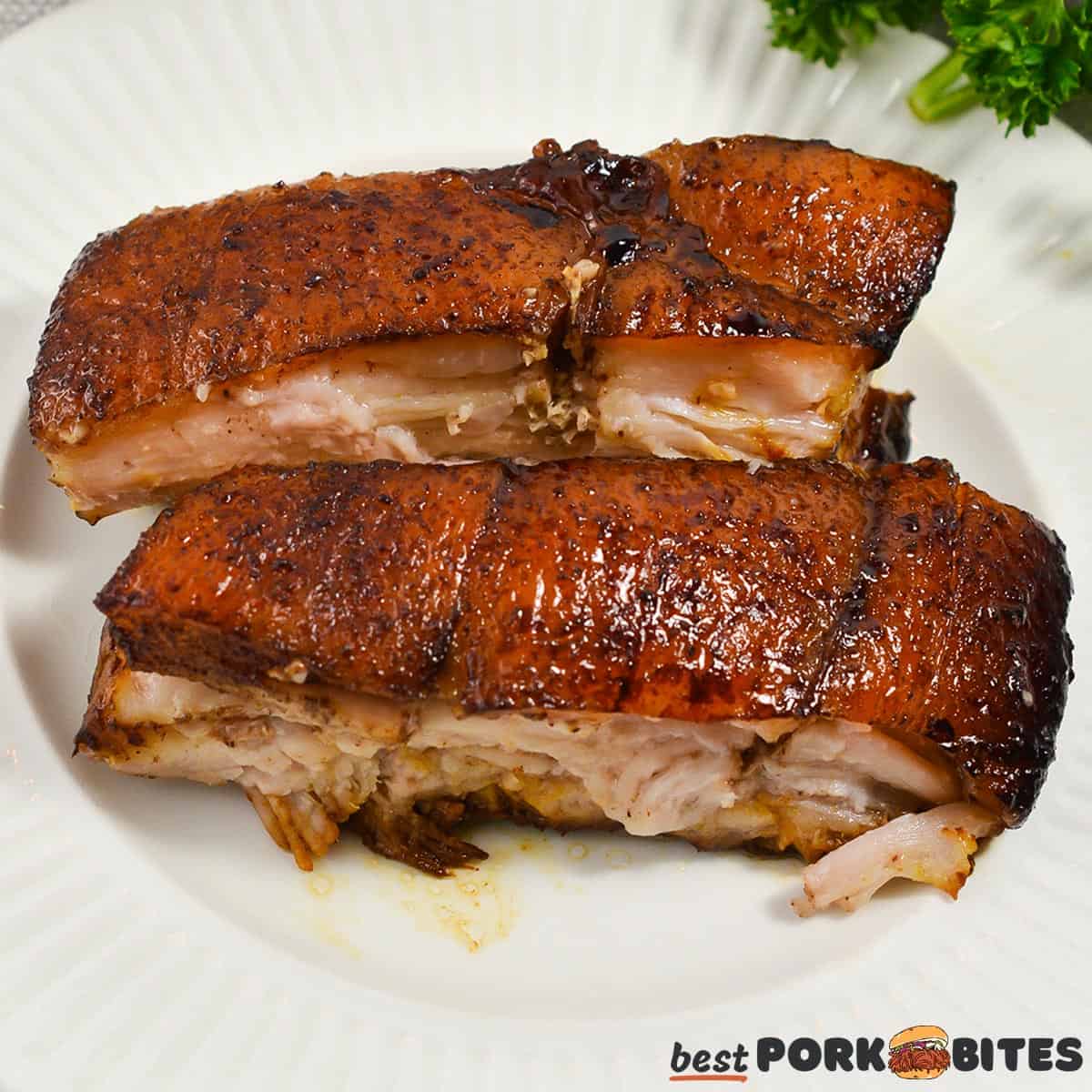 slices of roasted pork belly on a white plate with parsley