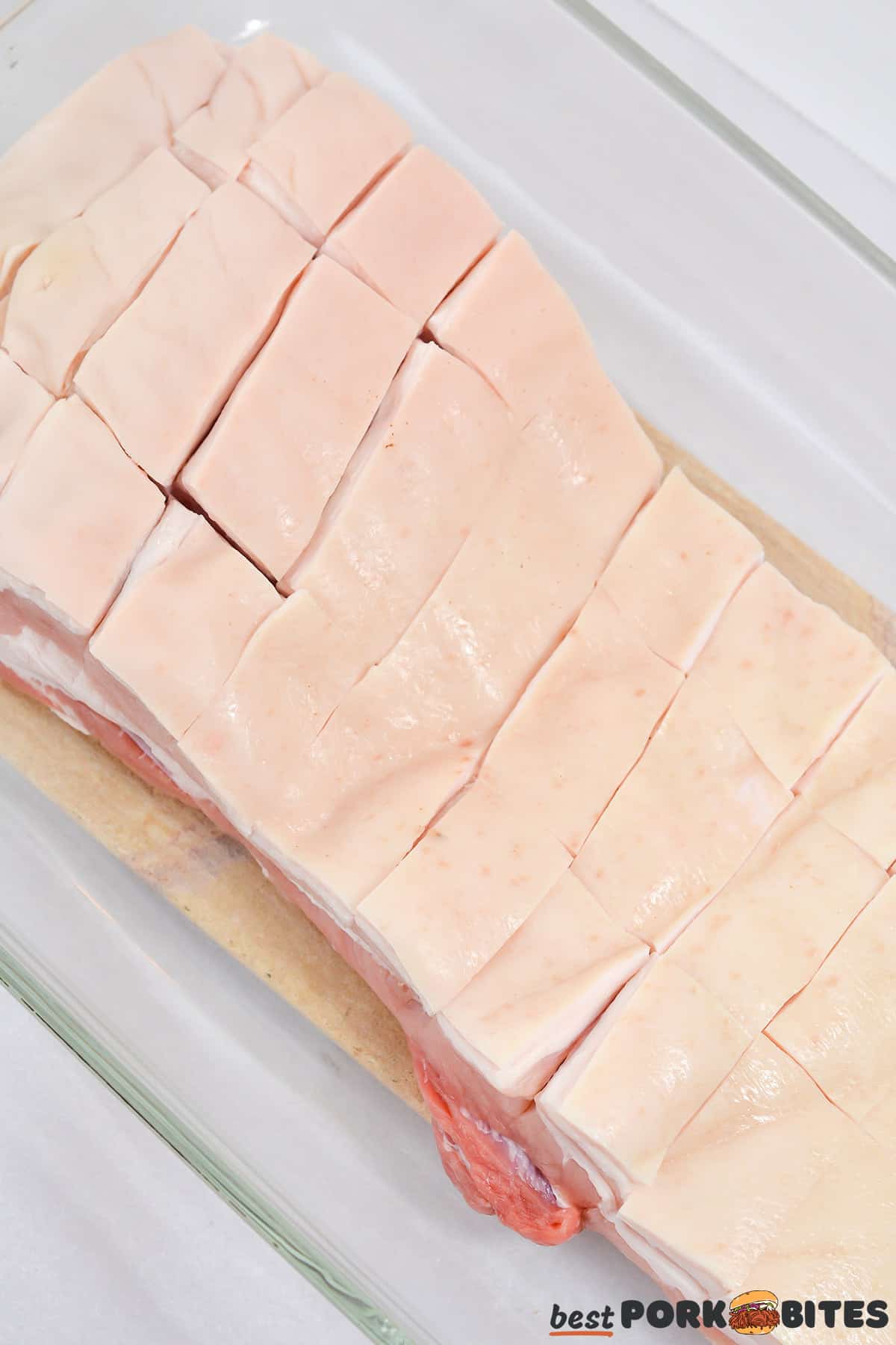 raw pork belly in a glass dish fat-side up with the fat scored by a knife