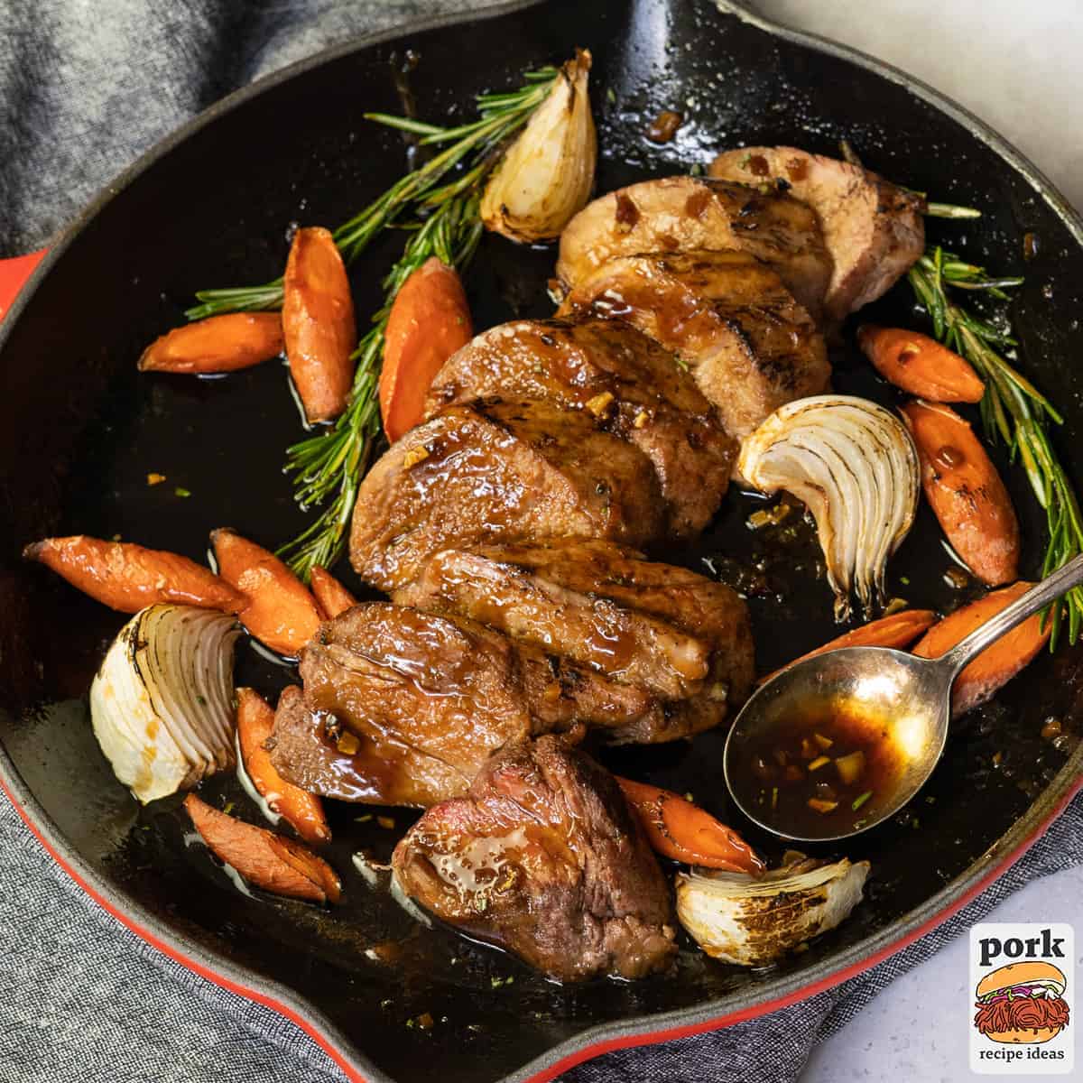 sliced roast pork tenderloin in a pan with garlic, carrots, and herbs