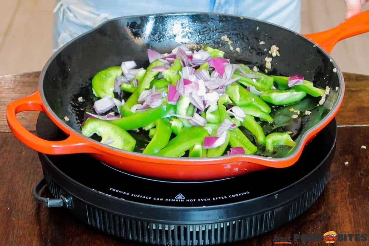 peppers and onions added to a skillet to saute