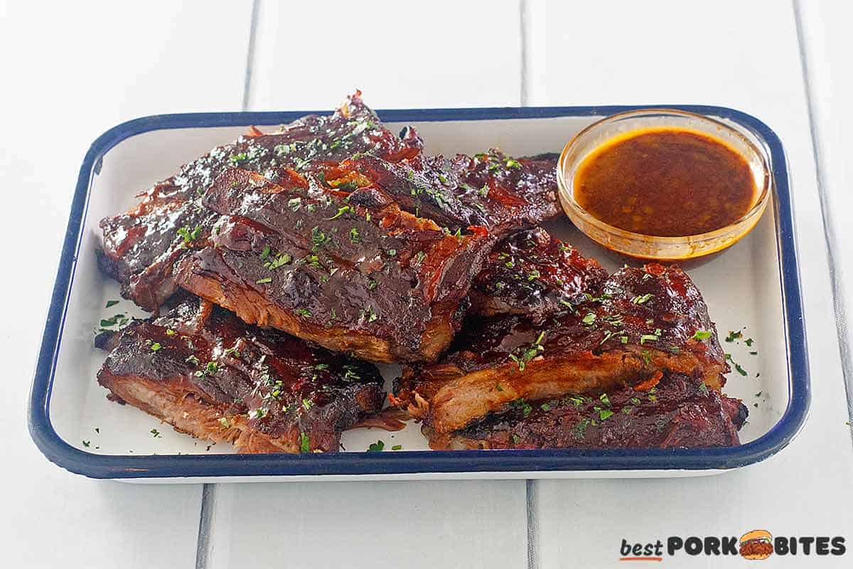 slow cooked spare ribs on a plate with a bowl of bbq sauce