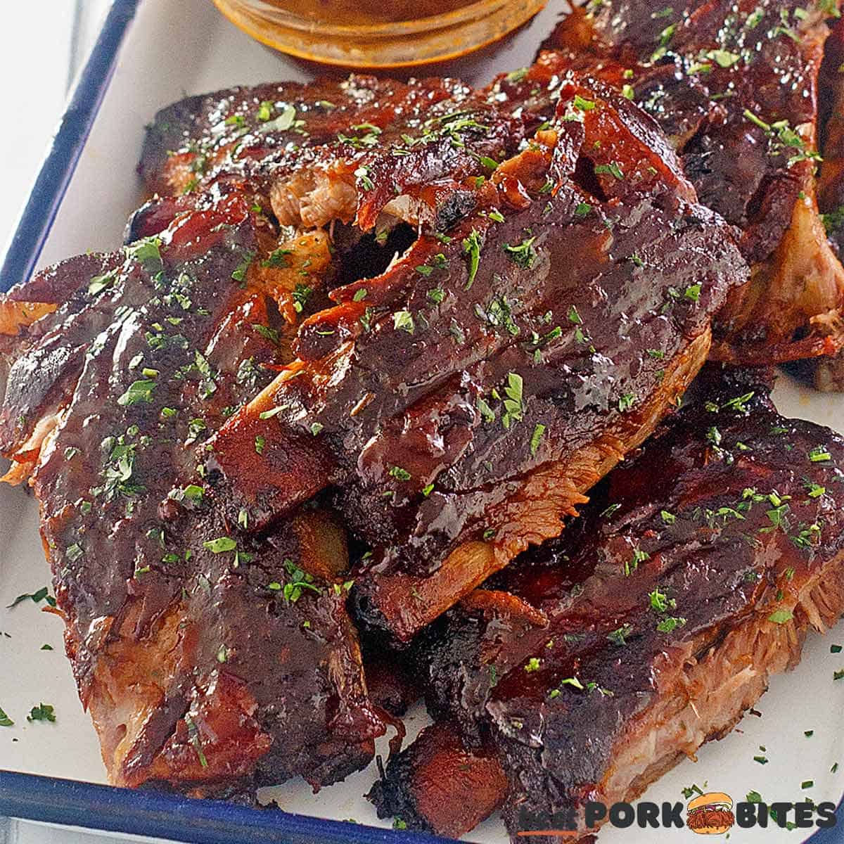 slow cooked pork ribs on a plate with bbq sauce in a bowl