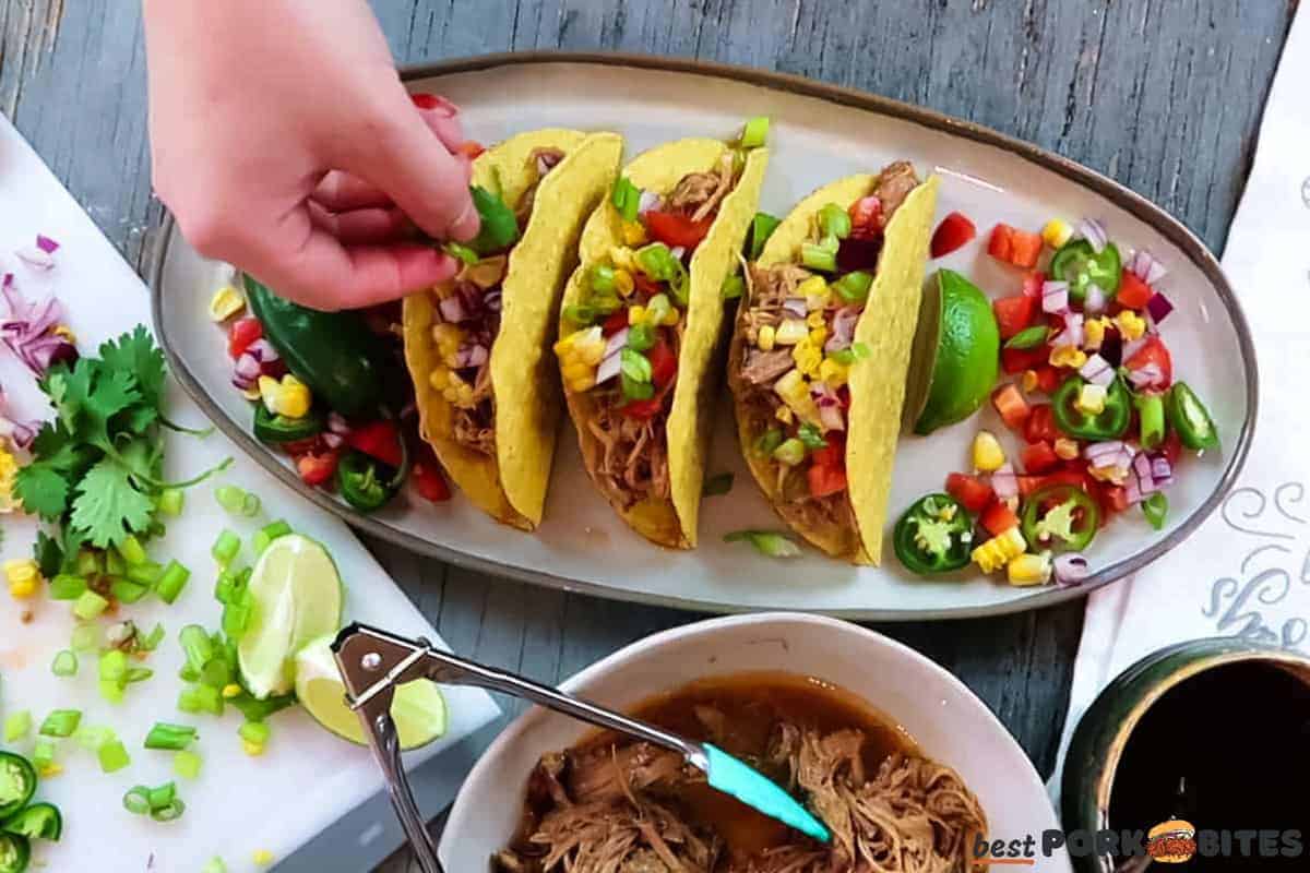 a handle sprinkling green onions on to a plate of slow cooker pork tacos