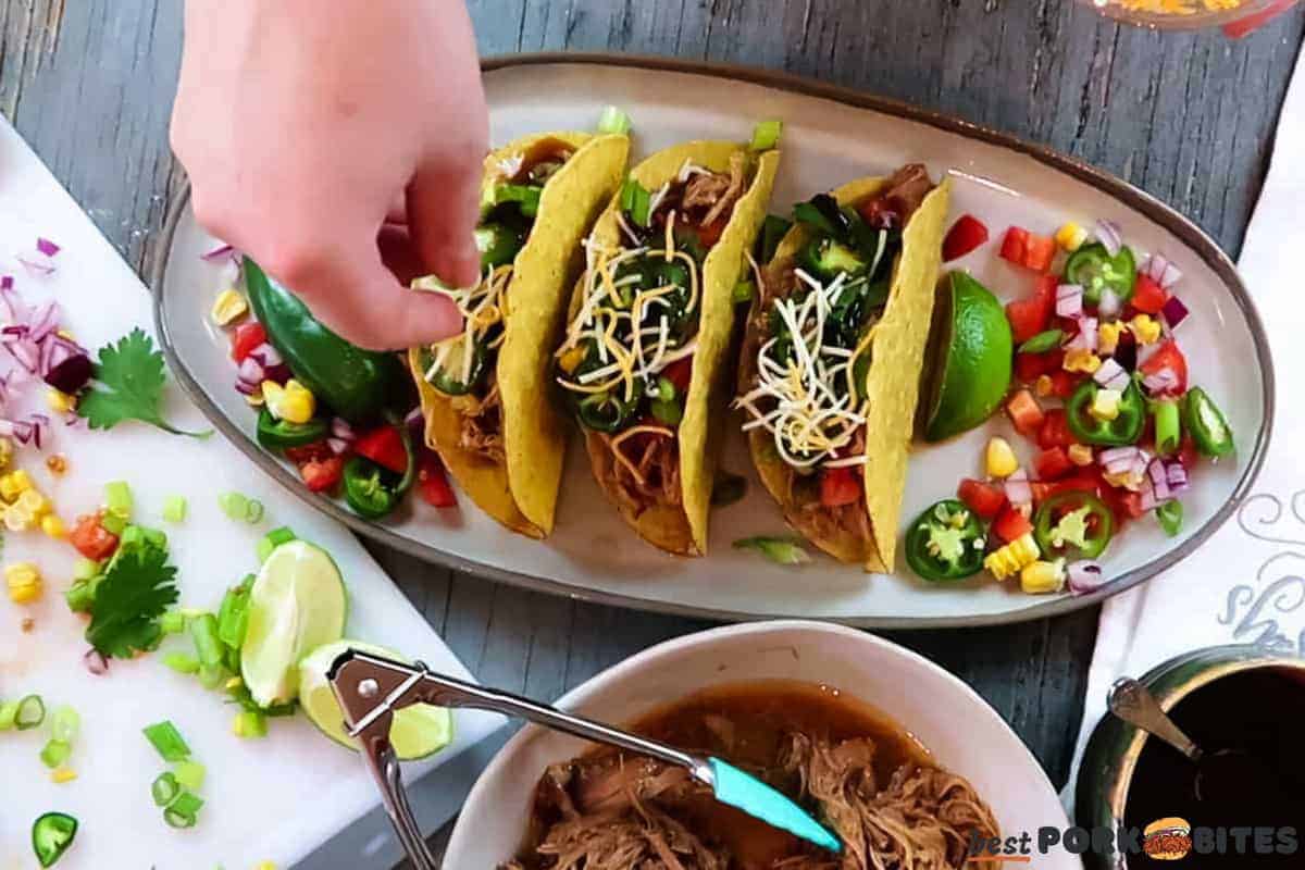a dish of pulled pork tacos with cheese being sprinkled on