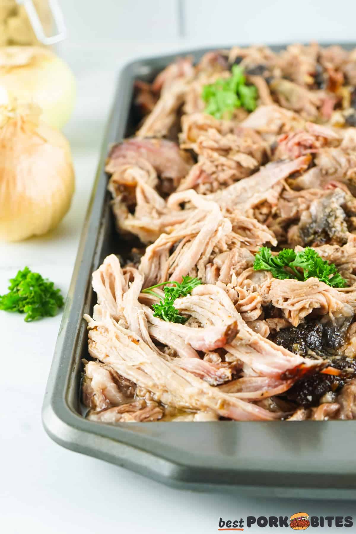 a baking tray on a counter full of shredded smoked pulled pork next to onions