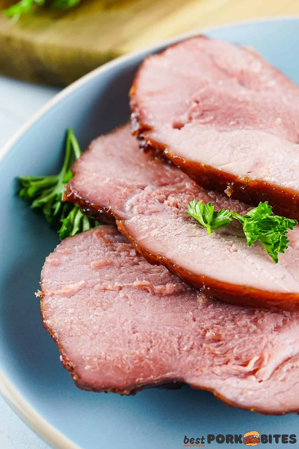 three slices of smoked ham on a blue plate with parsley garnish