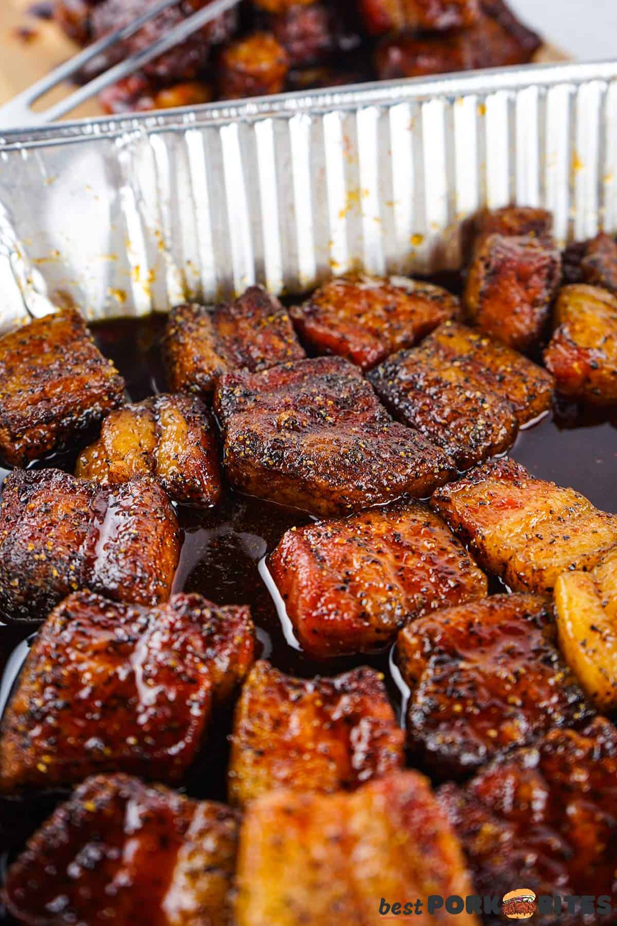 cooked pork belly burnt ends in a pan filled with sauce